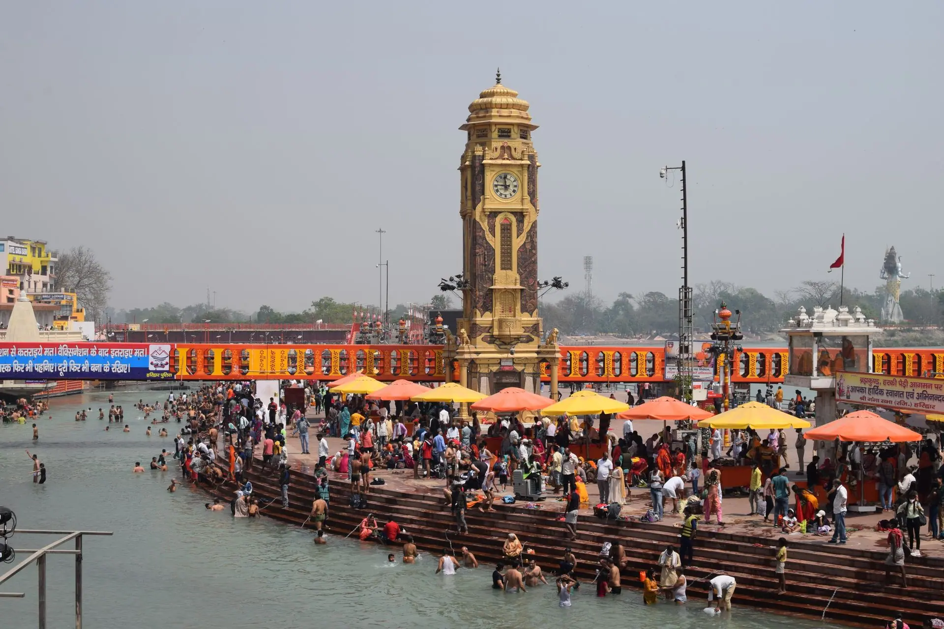 Vibrant scene of pilgrims bathing in Haridwar's Ganges with the iconic clock tower in view