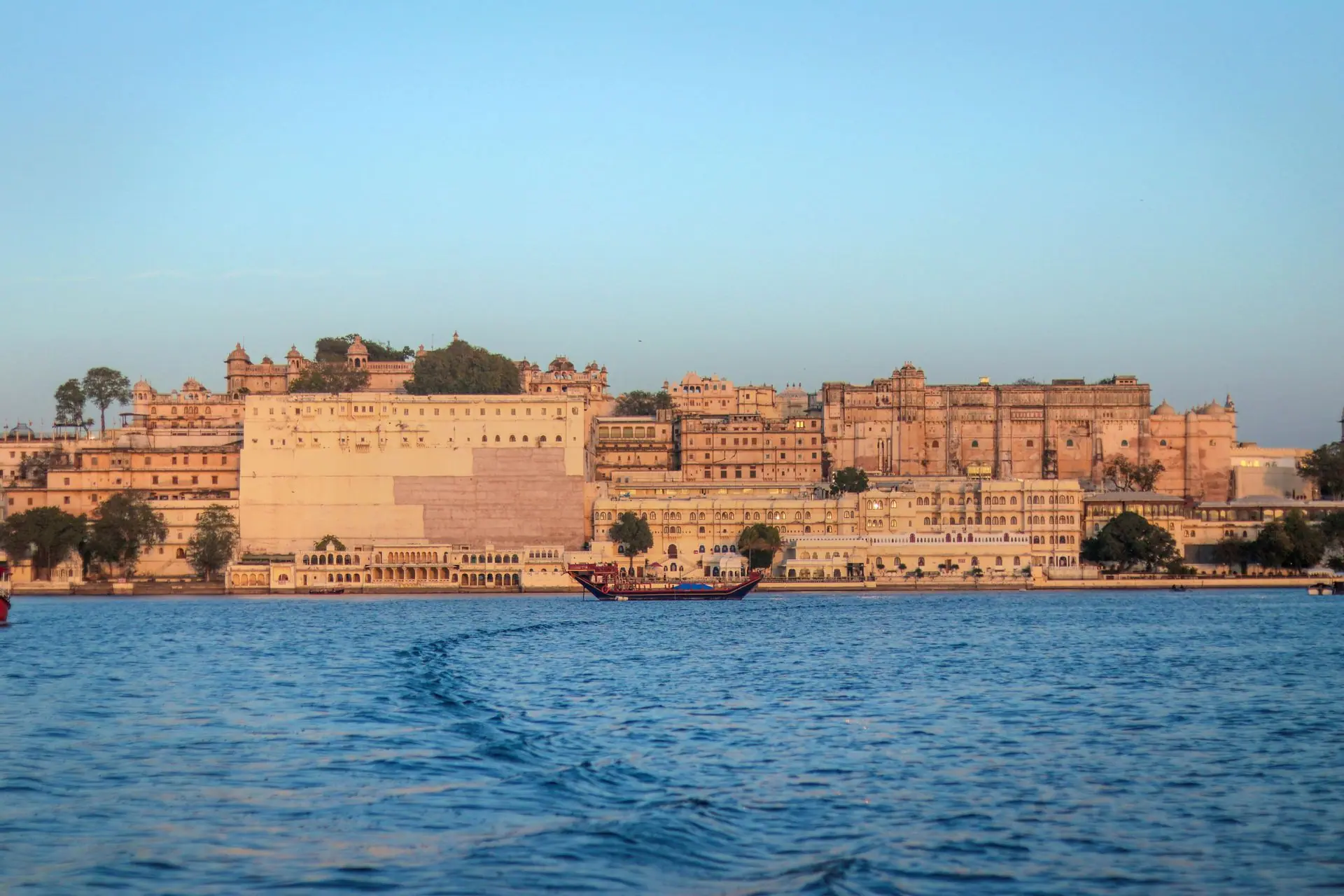 View of the historic Udaipur City Palace in Rajasthan, India, across Lake Pichola during sunset