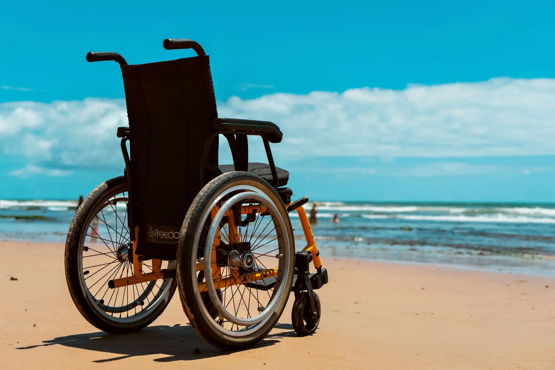 A wheelchair on a sandy beach overlooking the sea on a bright summer day