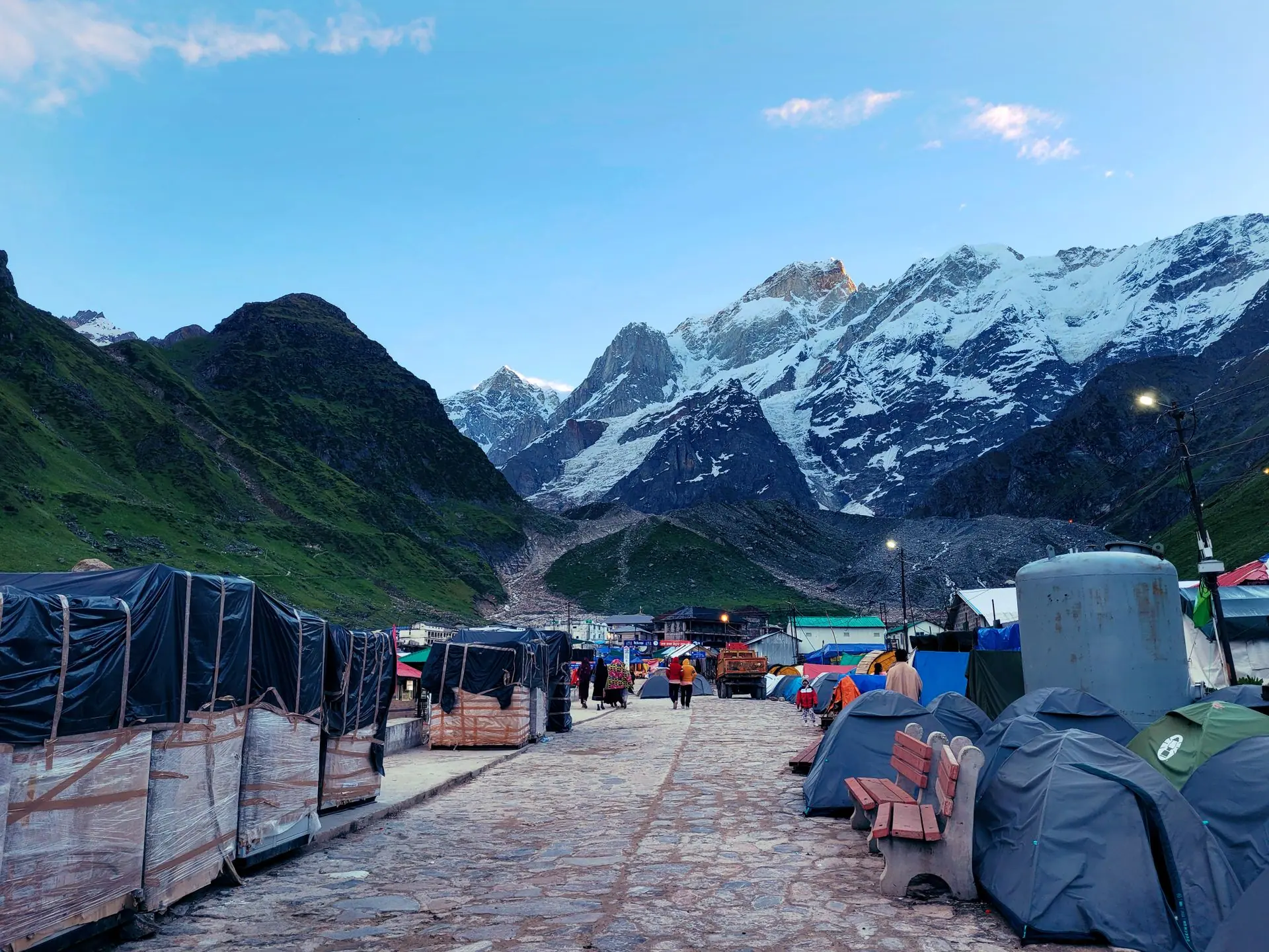 Picturesque Kedarnath setting with majestic snow-covered mountains and tents along a pathway