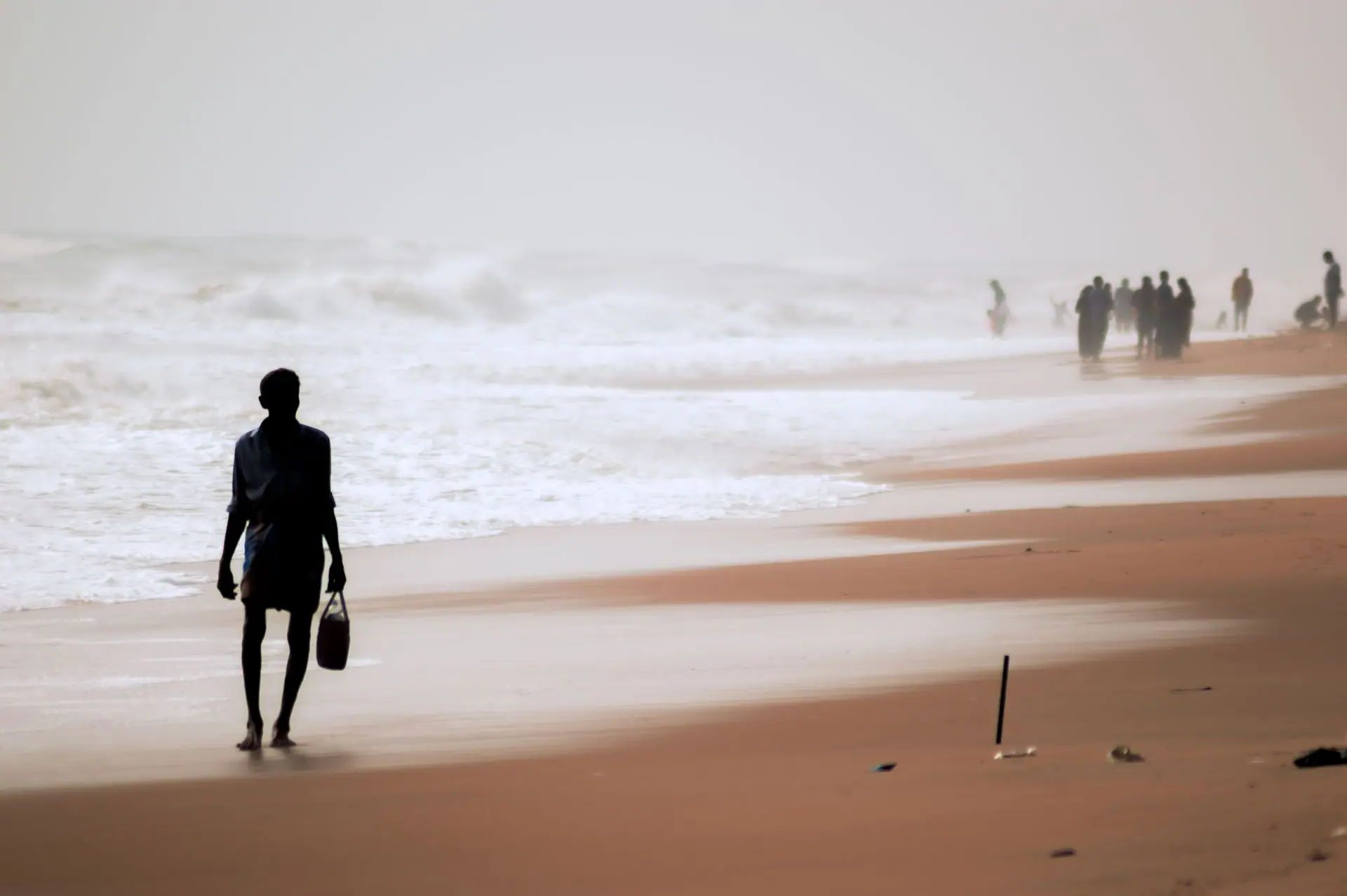 A silhouette of a man walking barefoot on the sandy beach of Chennai, India with ocean waves in the background