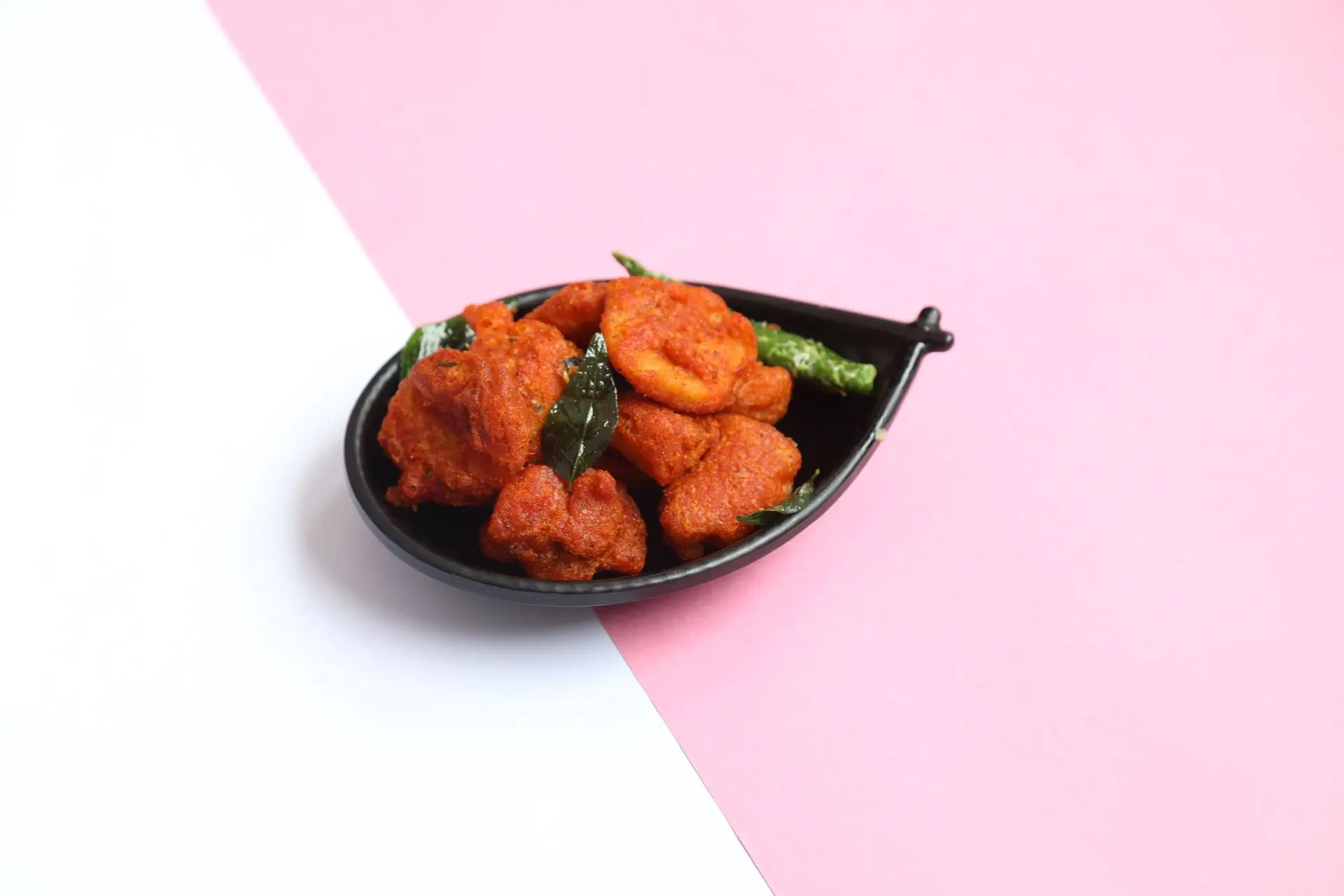 Tasty South Indian pakora served in a stylish black bowl against a vibrant pink and white backdrop, ideal for food concepts