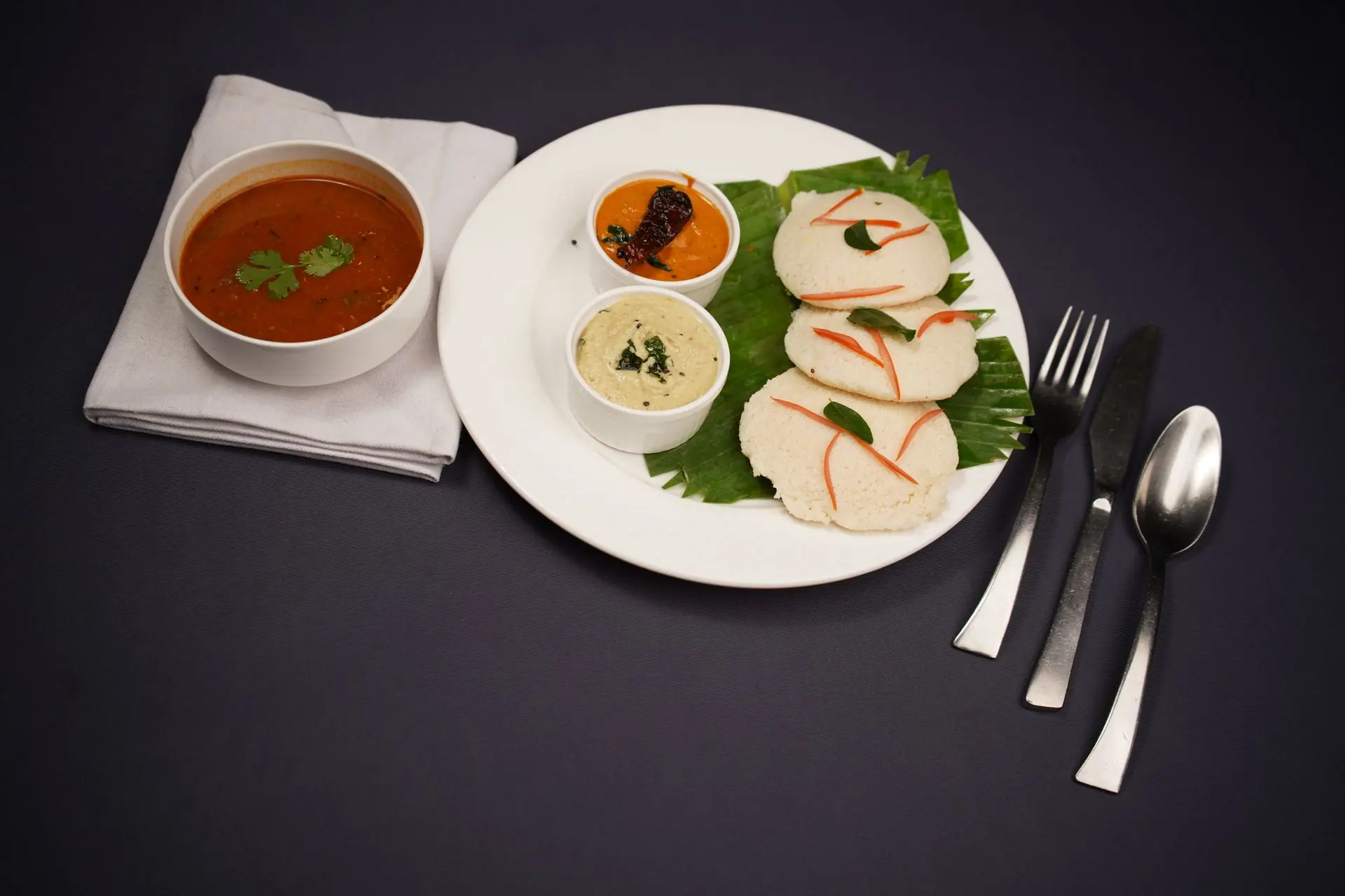 High angle view of South Indian idli, chutneys, and sambhar on a black background