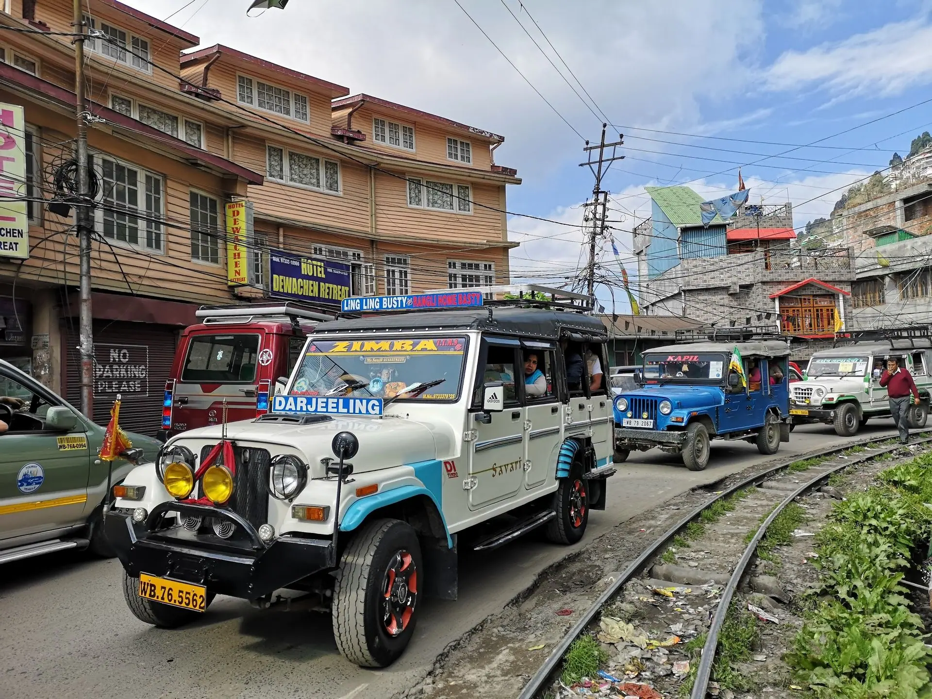 A convoy of jeeps driving on a busy street alongside railway tracks in Darjeeling