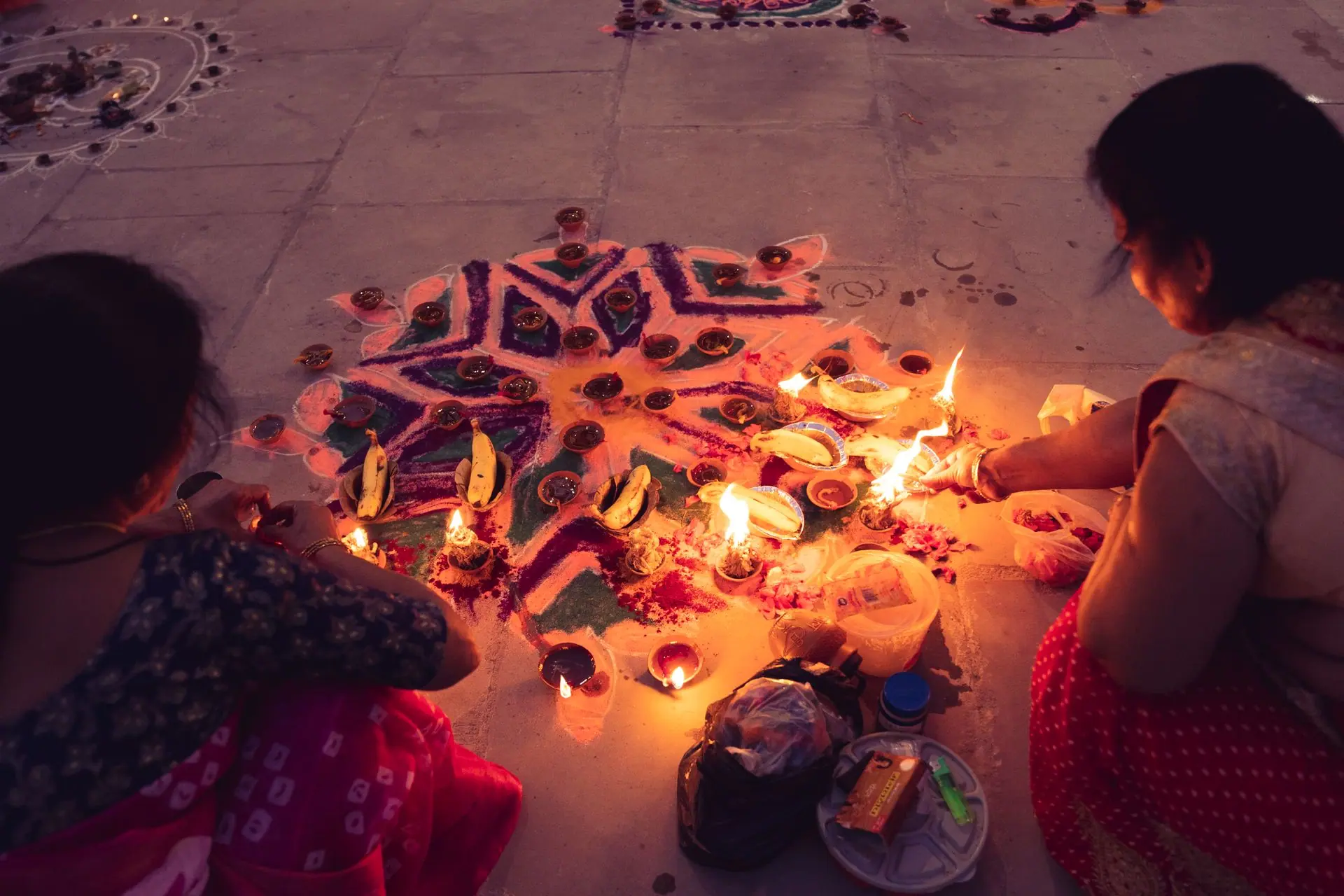 Two women create a colorful rangoli and light diyas for Diwali celebration, showcasing Indian culture and tradition