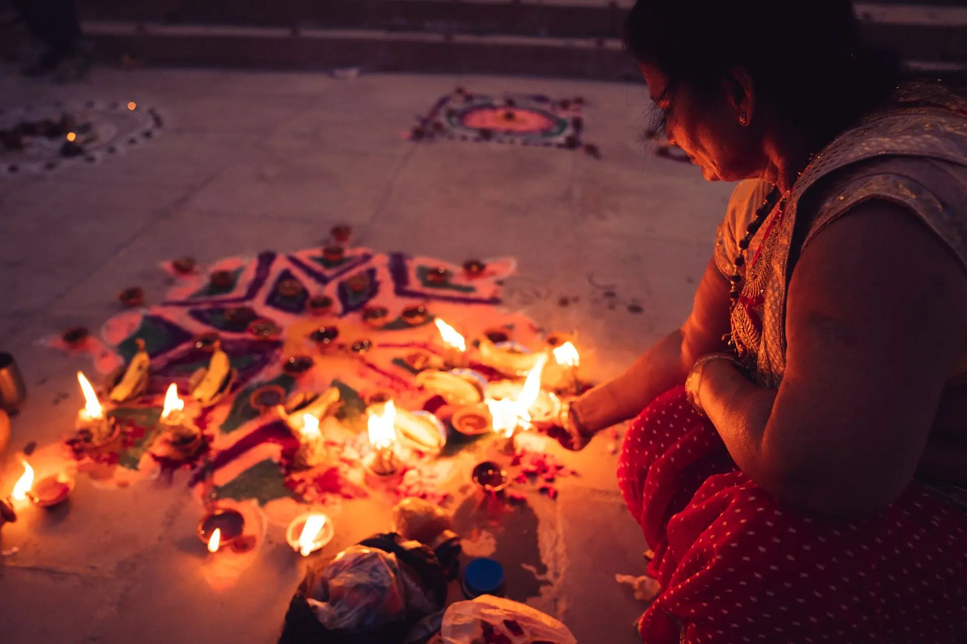 A woman celebrates a traditional Indian festival with rangoli and candles lighting the night