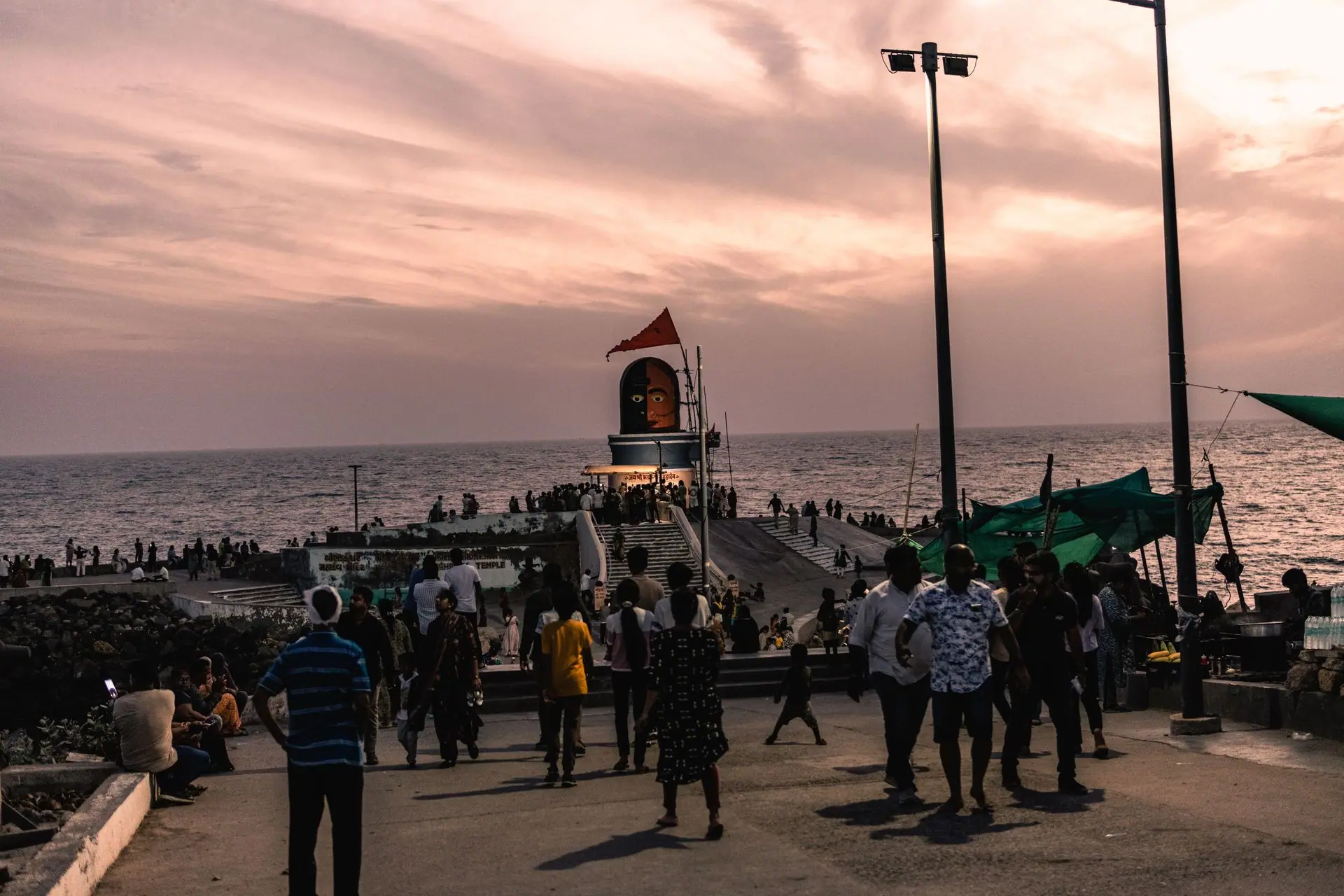 Crowds gather at sunset by the sea pier in Dwarka, India, under a colorful sky