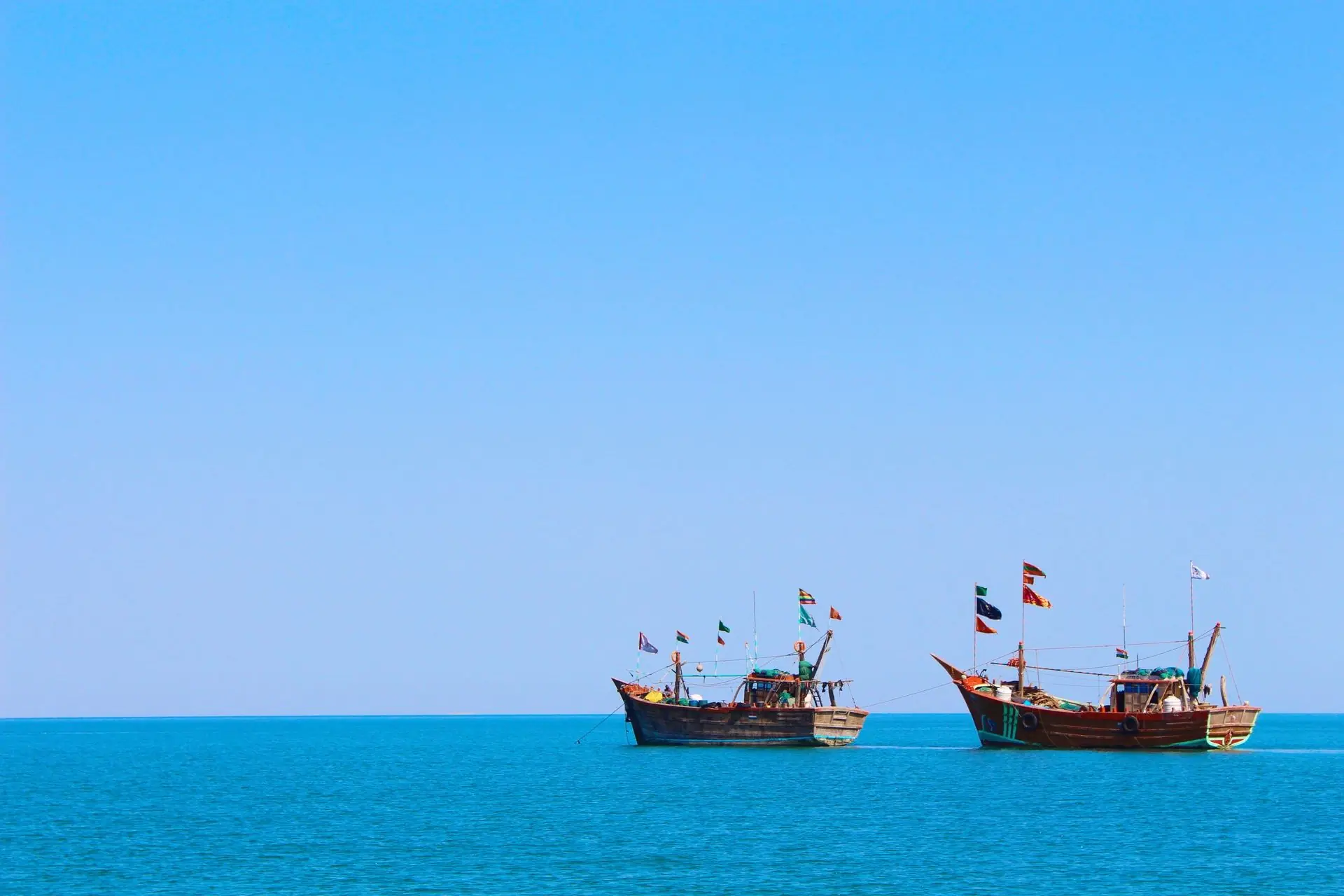 Two traditional wooden boats with flags on the Arabian Sea under a clear blue sky in Dwarka, India
