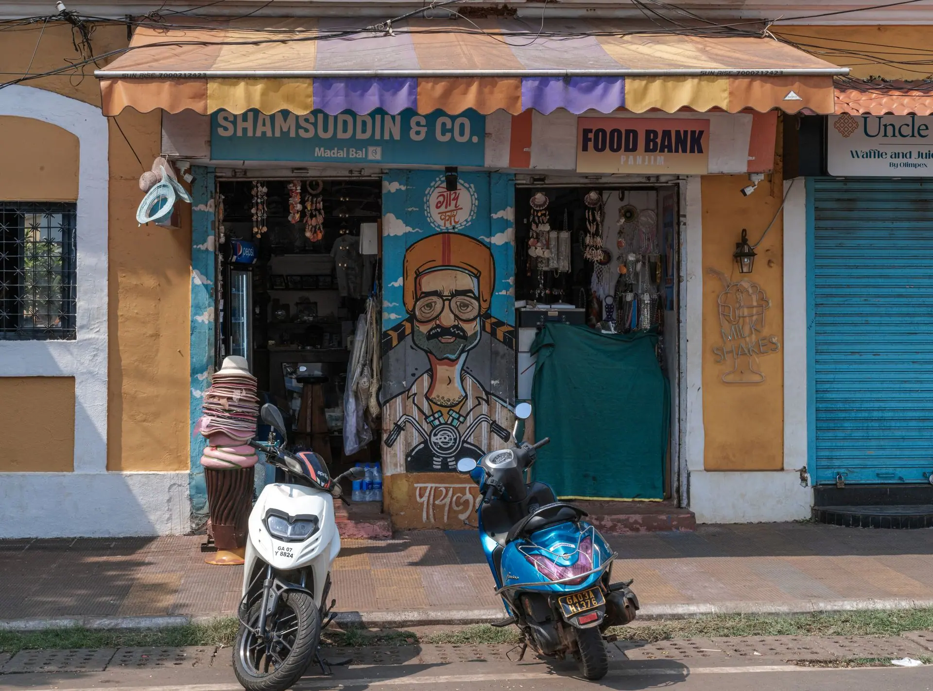 A vibrant street shop in Panaji, Goa with painted shutters and parked scooters, exuding local culture