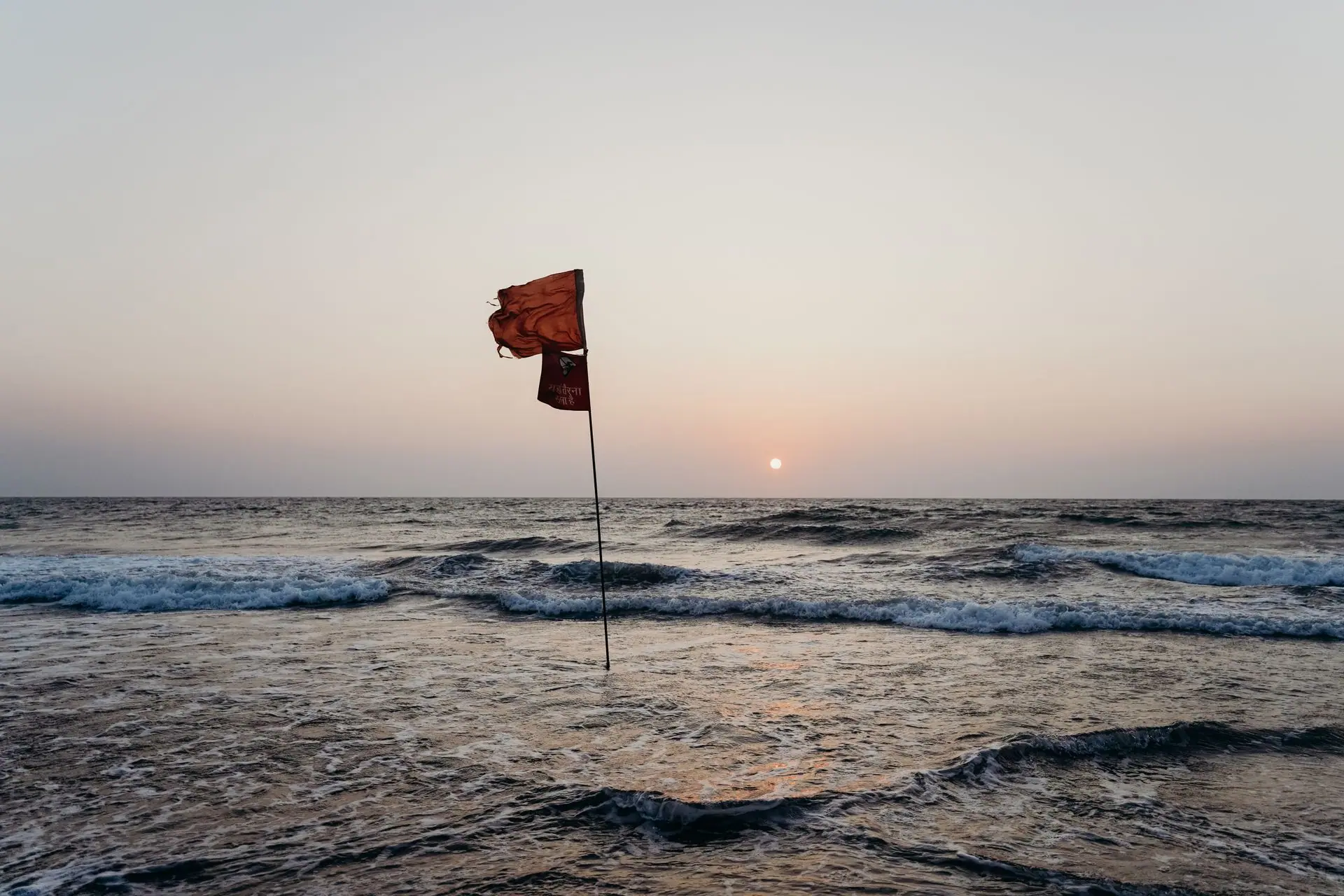 A red flag waves on a tranquil Goan beach at sunset, overlooking the serene ocean