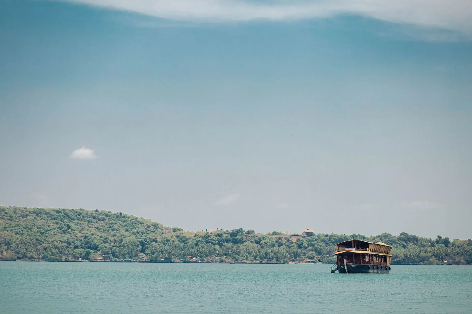A serene view of a boat on the calm waters of Goa, surrounded by lush greenery
