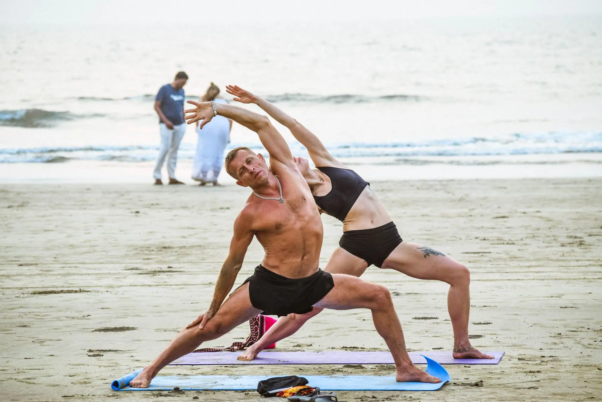 Two people practicing yoga on the tranquil Arambol Beach in Goa, India