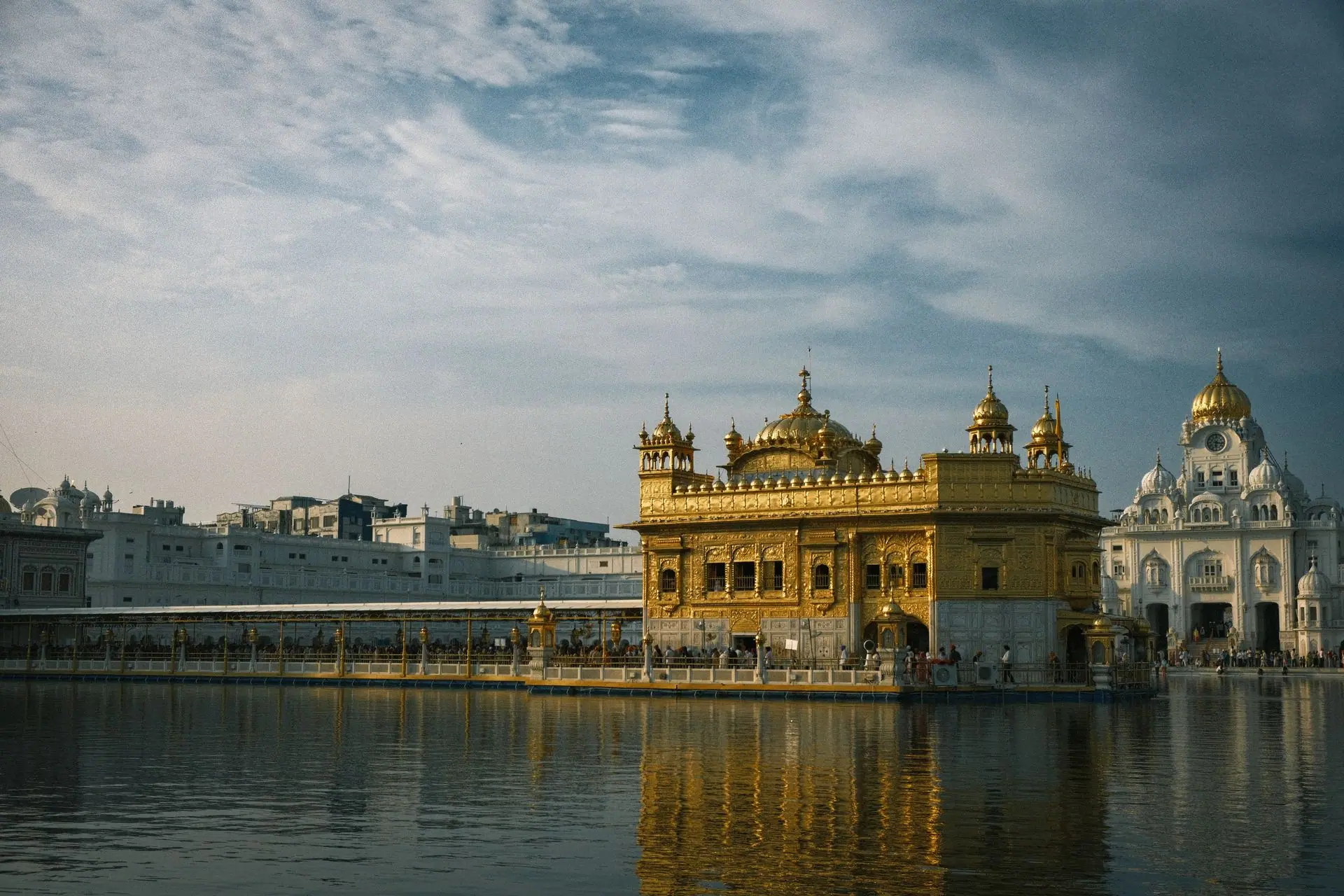 Stunning view of the Golden Temple in Amritsar at daytime, reflecting in calm waters with a blue sky backdrop