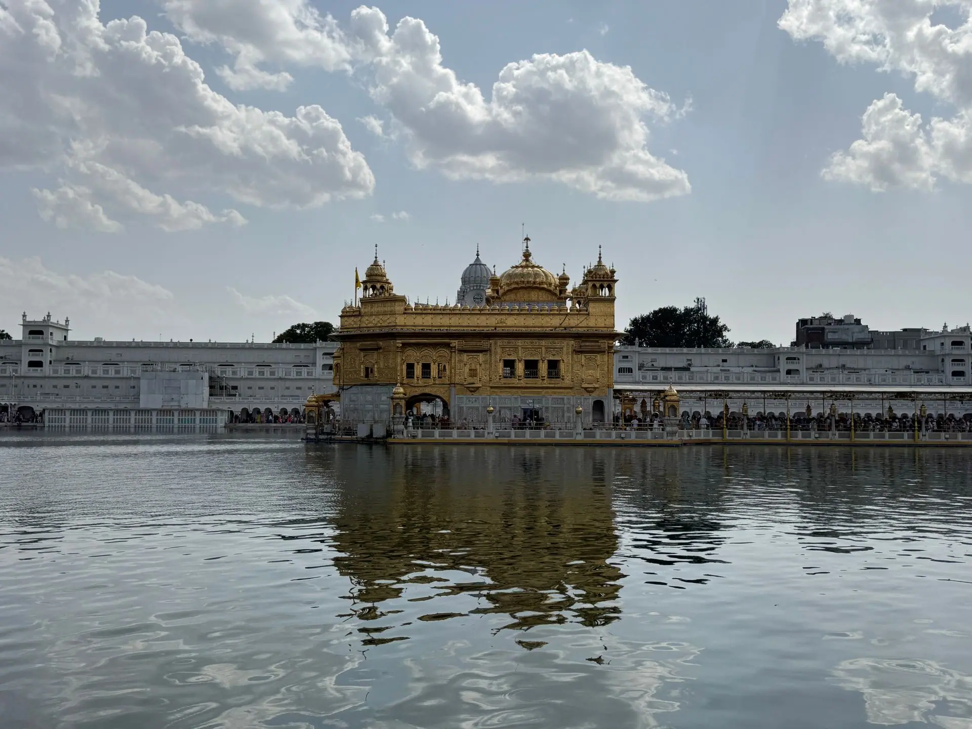 Stunning view of the Golden Temple reflecting in water under a bright, cloudy sky in Amritsar, India