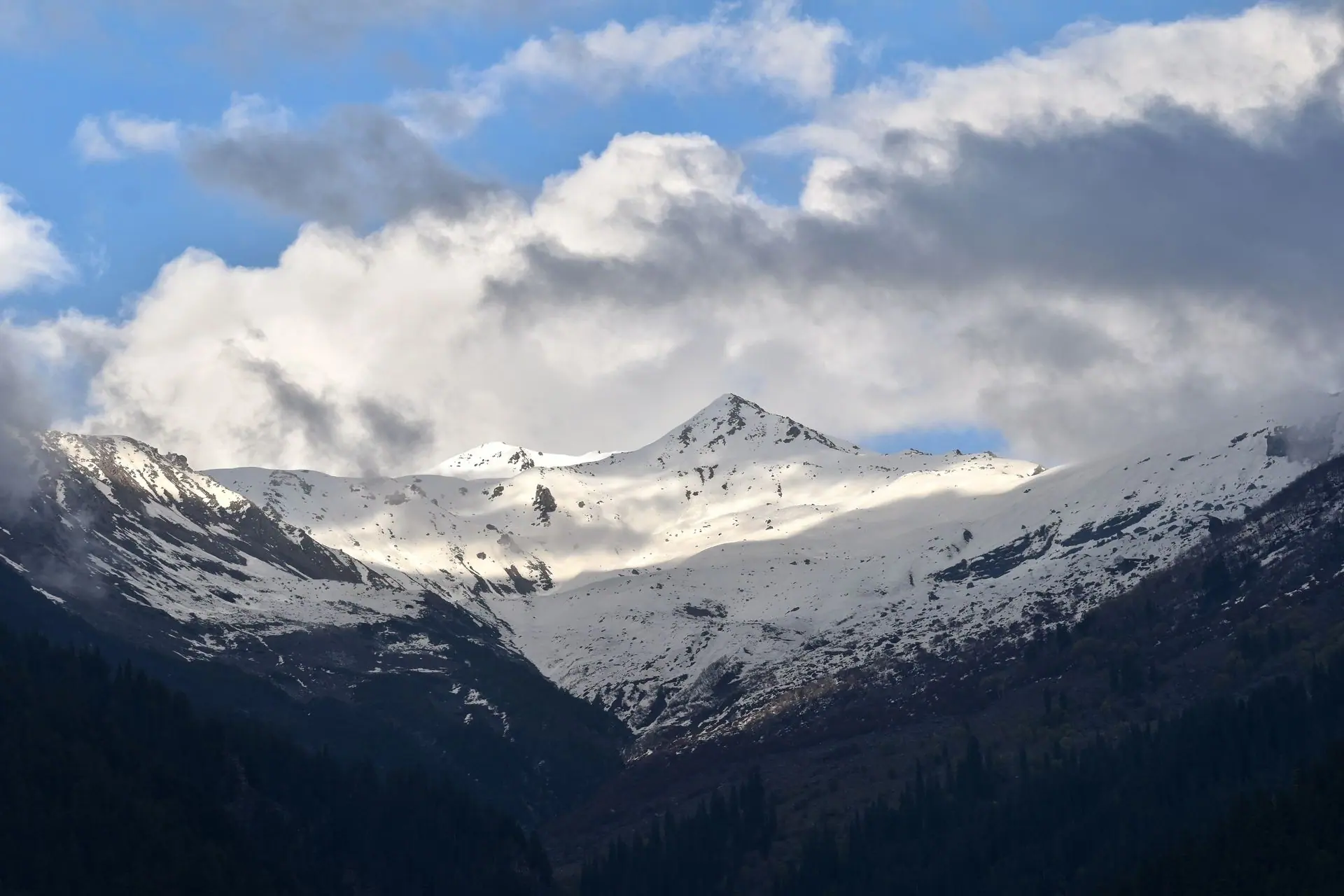 Stunning view of snow-covered mountains in Manali, HP, India under dramatic clouds and blue sky