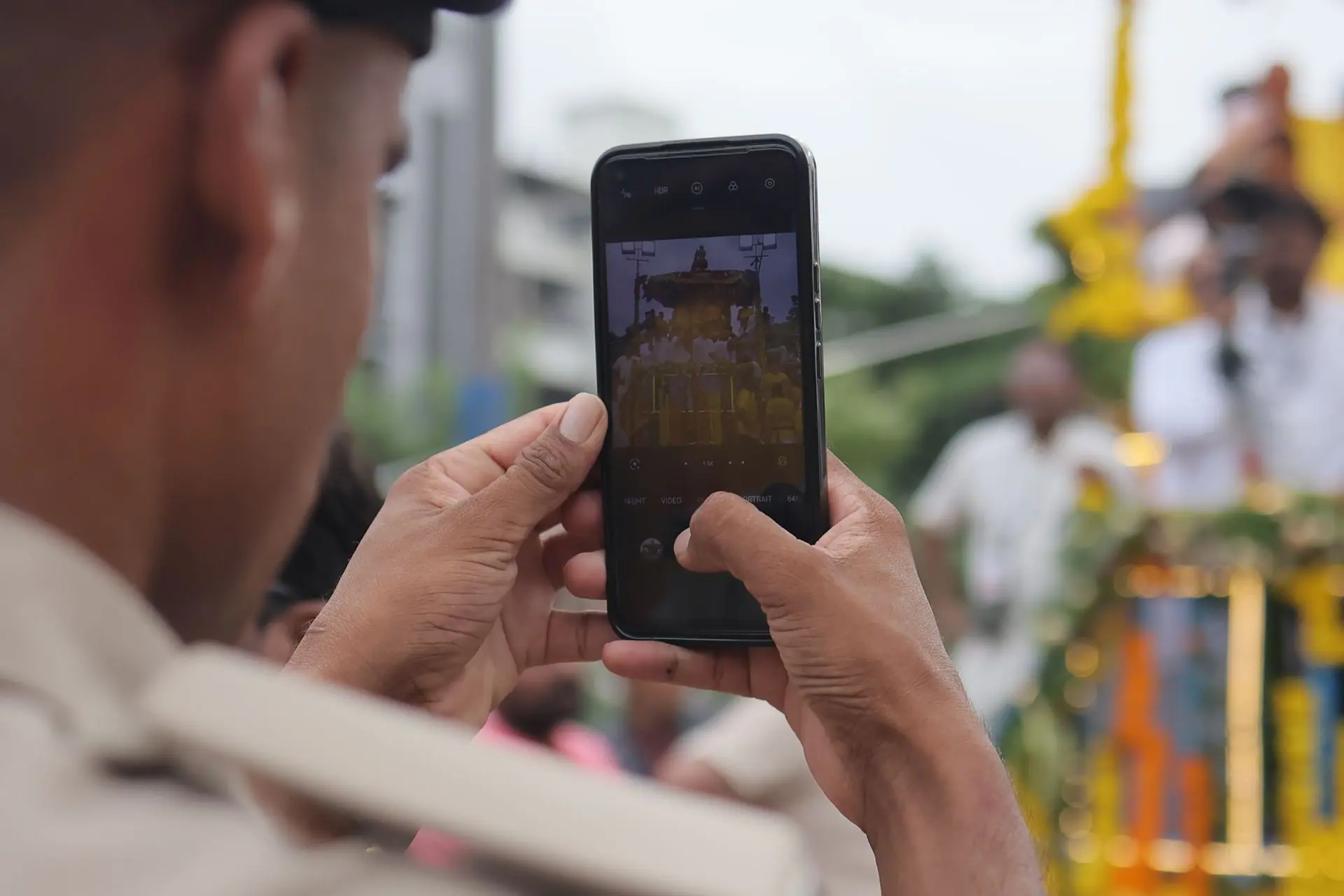 A person photographs the colorful Jagannath Rath Yatra parade with a smartphone