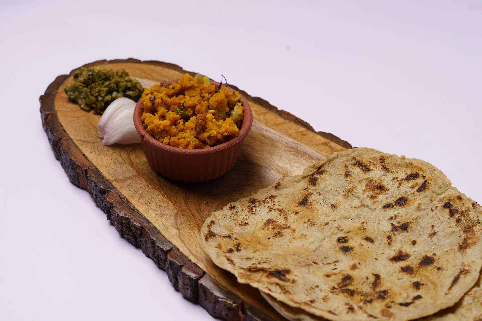 A traditional Indian thali featuring flatbread, spiced curry, chutney, and garlic on a wooden plate