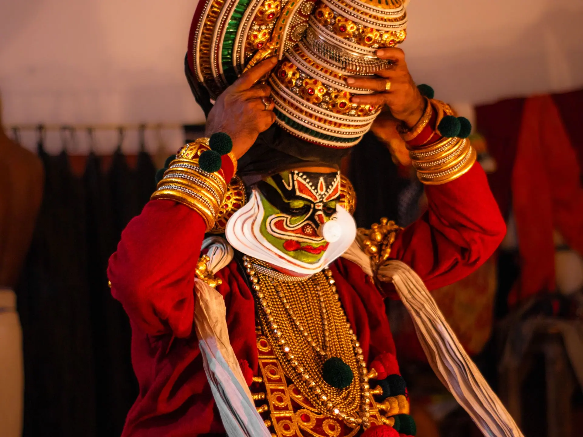 A vibrant Kathakali performer adjusts his ornate headpiece backstage, showcasing traditional Indian dance costume