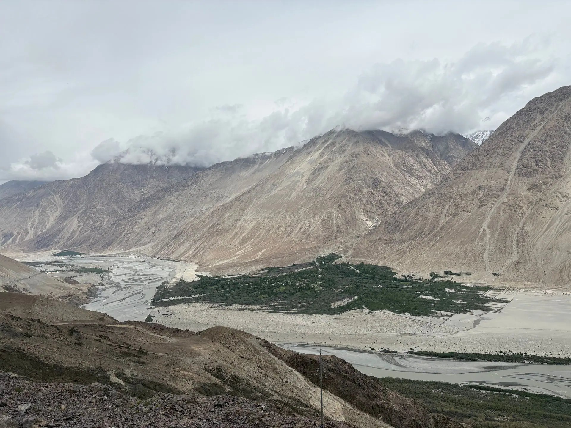 Stunning panoramic view of Nubra Valley's rugged mountains and lush green oasis under a cloudy sky