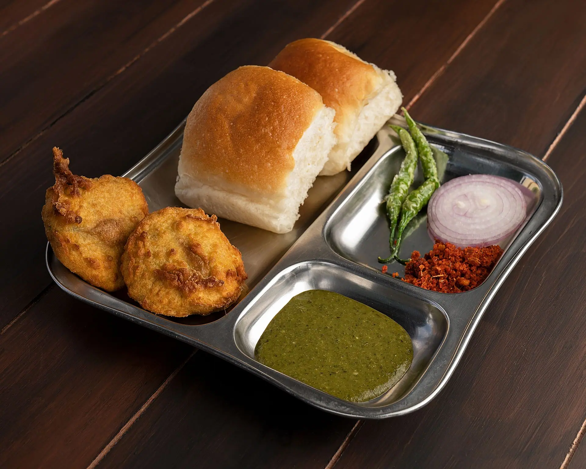 Delicious Maharashtrian Vada Pav served with chutney and spices on a stainless steel plate