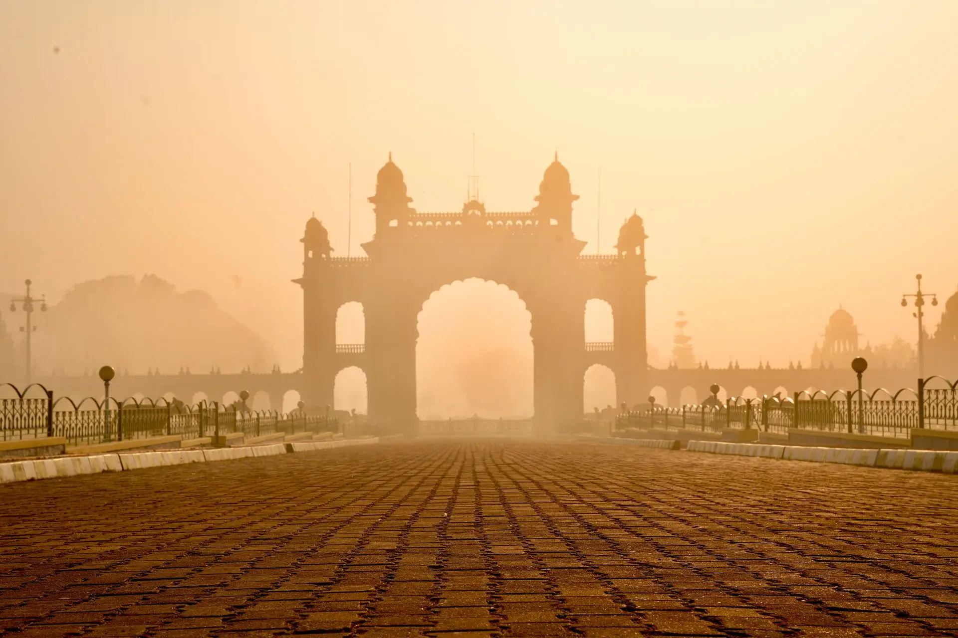 The Mysore Palace gate stands majestically enveloped in a golden morning fog, showcasing elegant 18th-century architecture