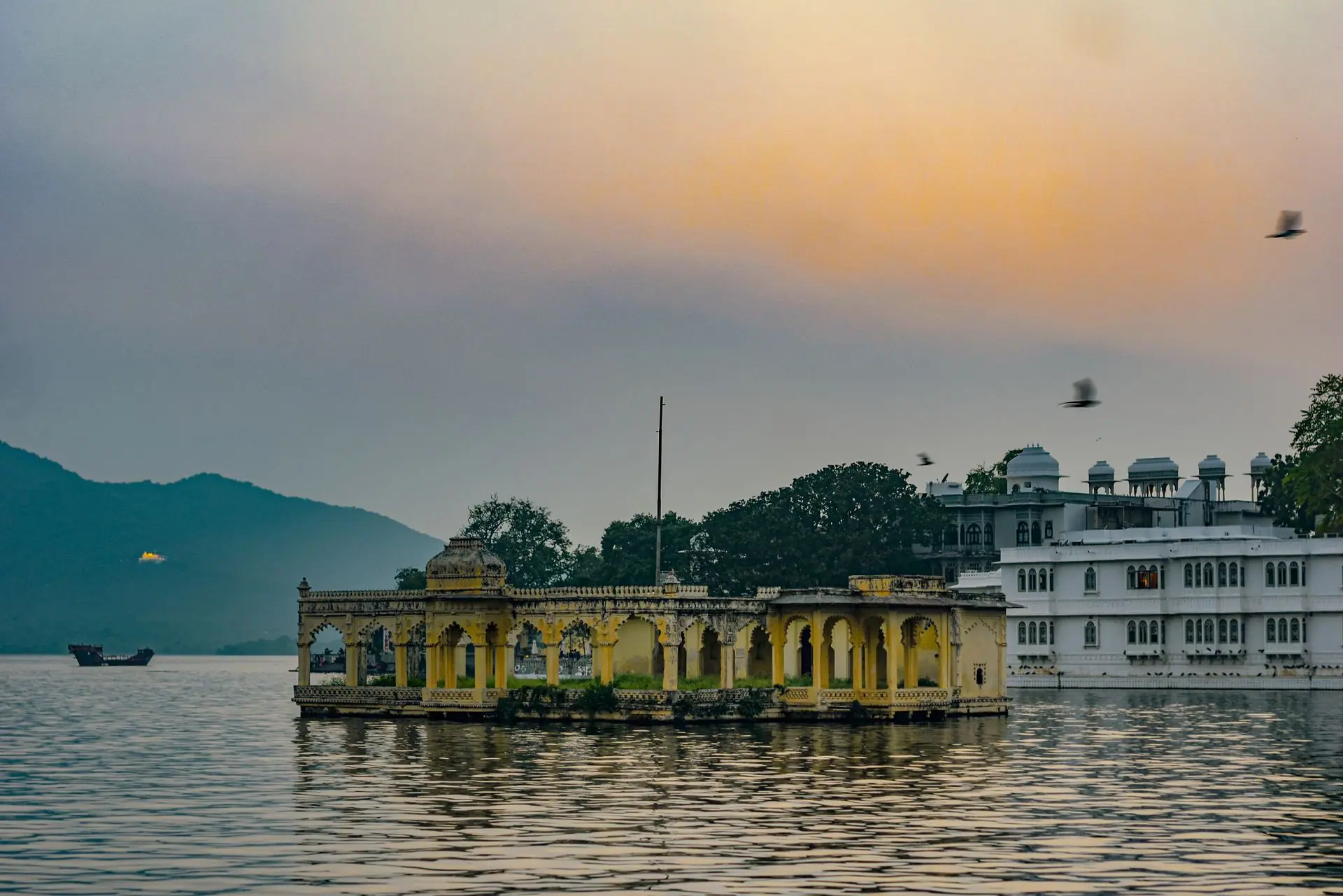 A serene view of a Lake Palace in India with a vibrant sunset sky and birds in flight