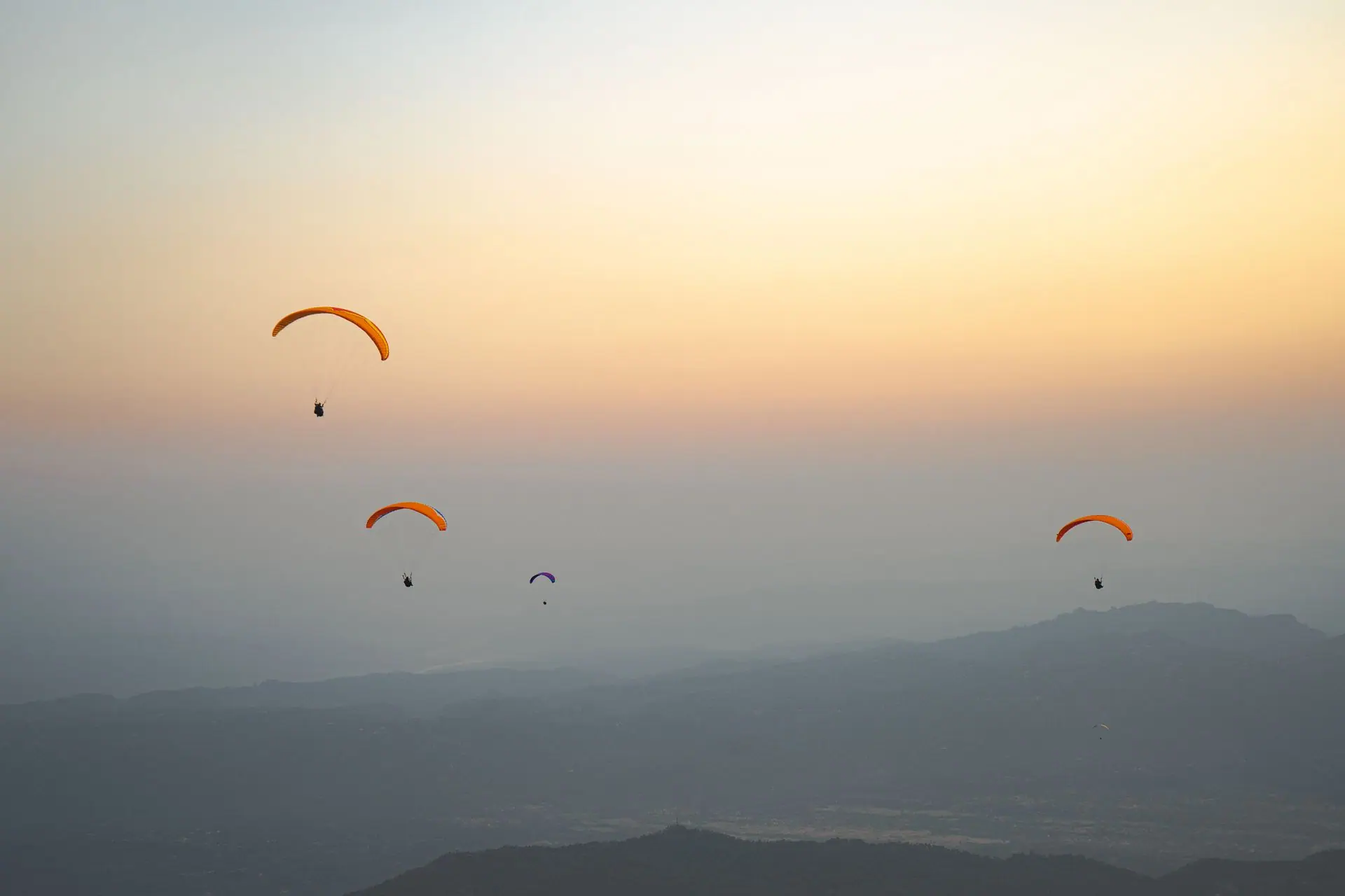 Paragliders gracefully fly over Bir, India during a stunning sunset, capturing an adventurous spirit
