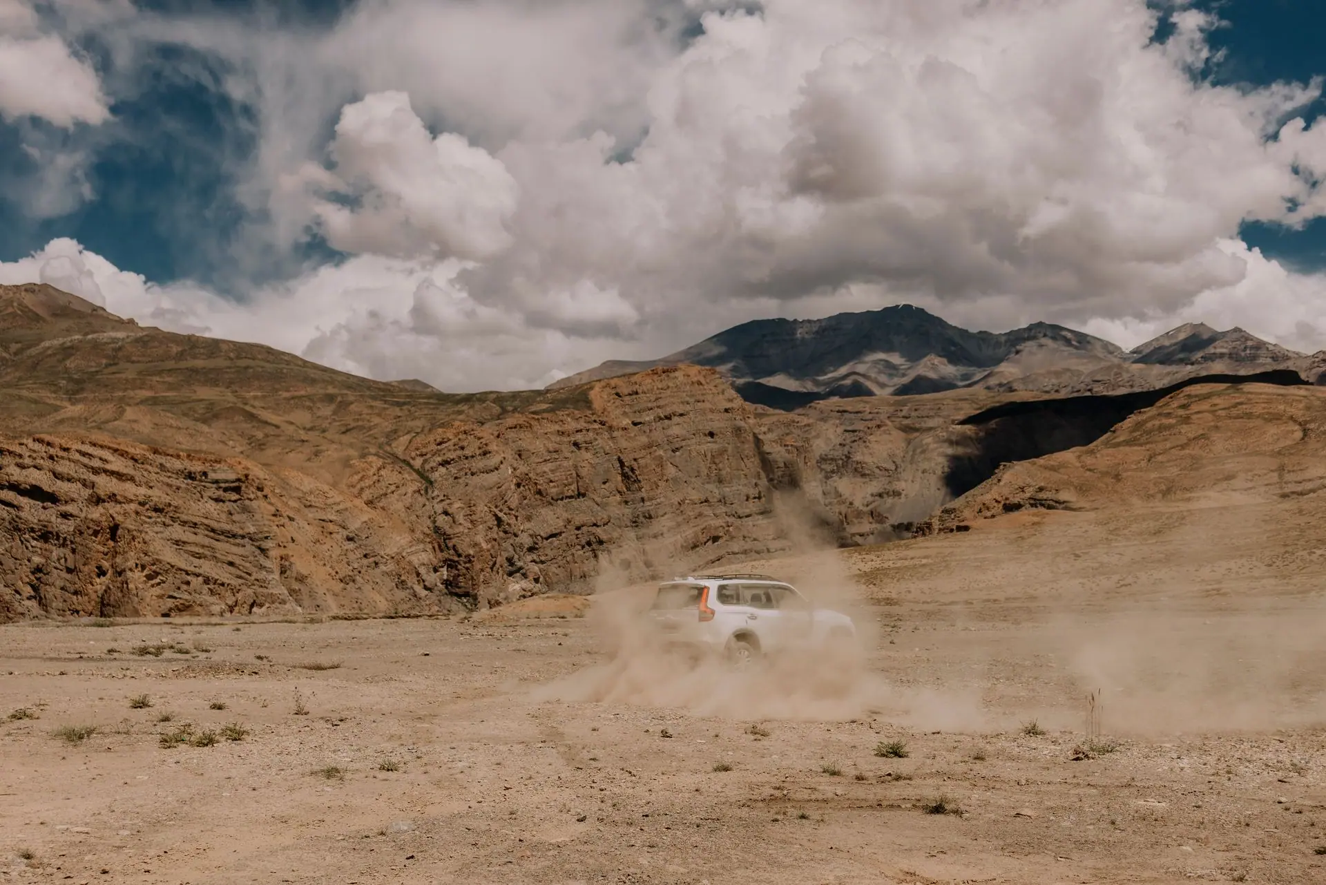 A car kicks up dust while off-roading in the rugged terrain of Spiti Valley