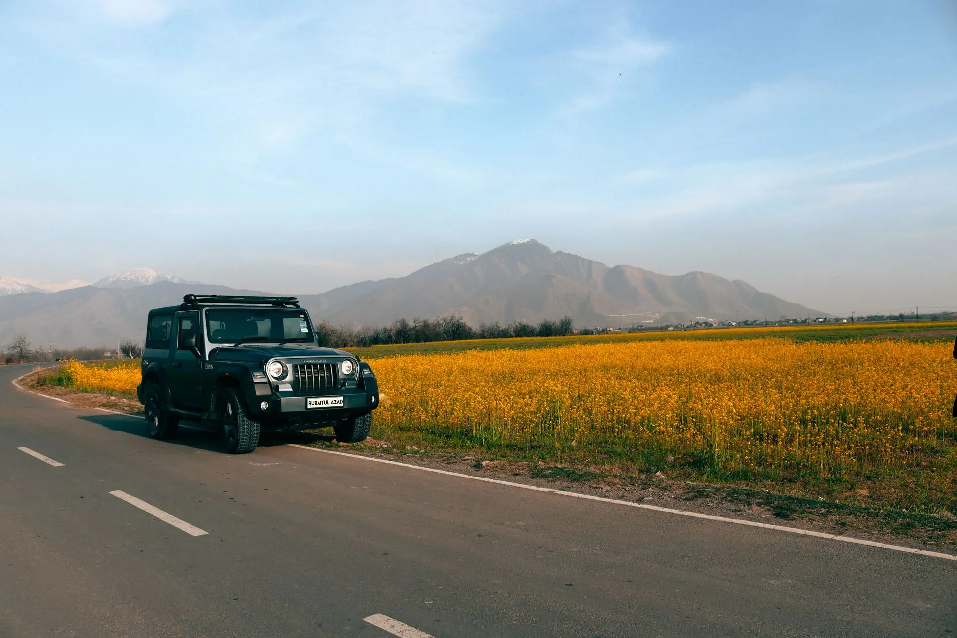 Mahindra Thar parked by a vibrant yellow field under a clear blue sky in Kashmir, India