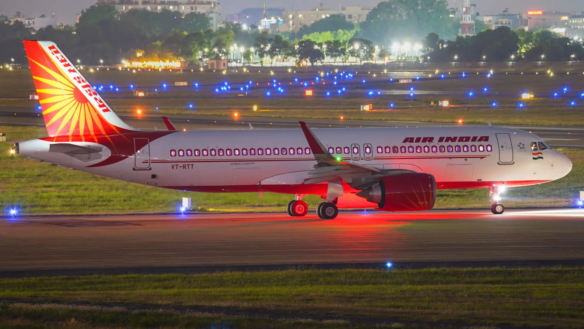 Air India Airbus A320 on the illuminated runway of an airport at night, showcasing its vibrant red and white design