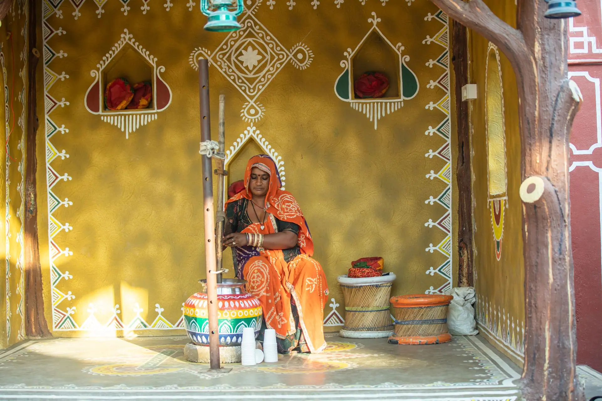 A Rajasthani woman in traditional attire churning butter in a culturally decorated space