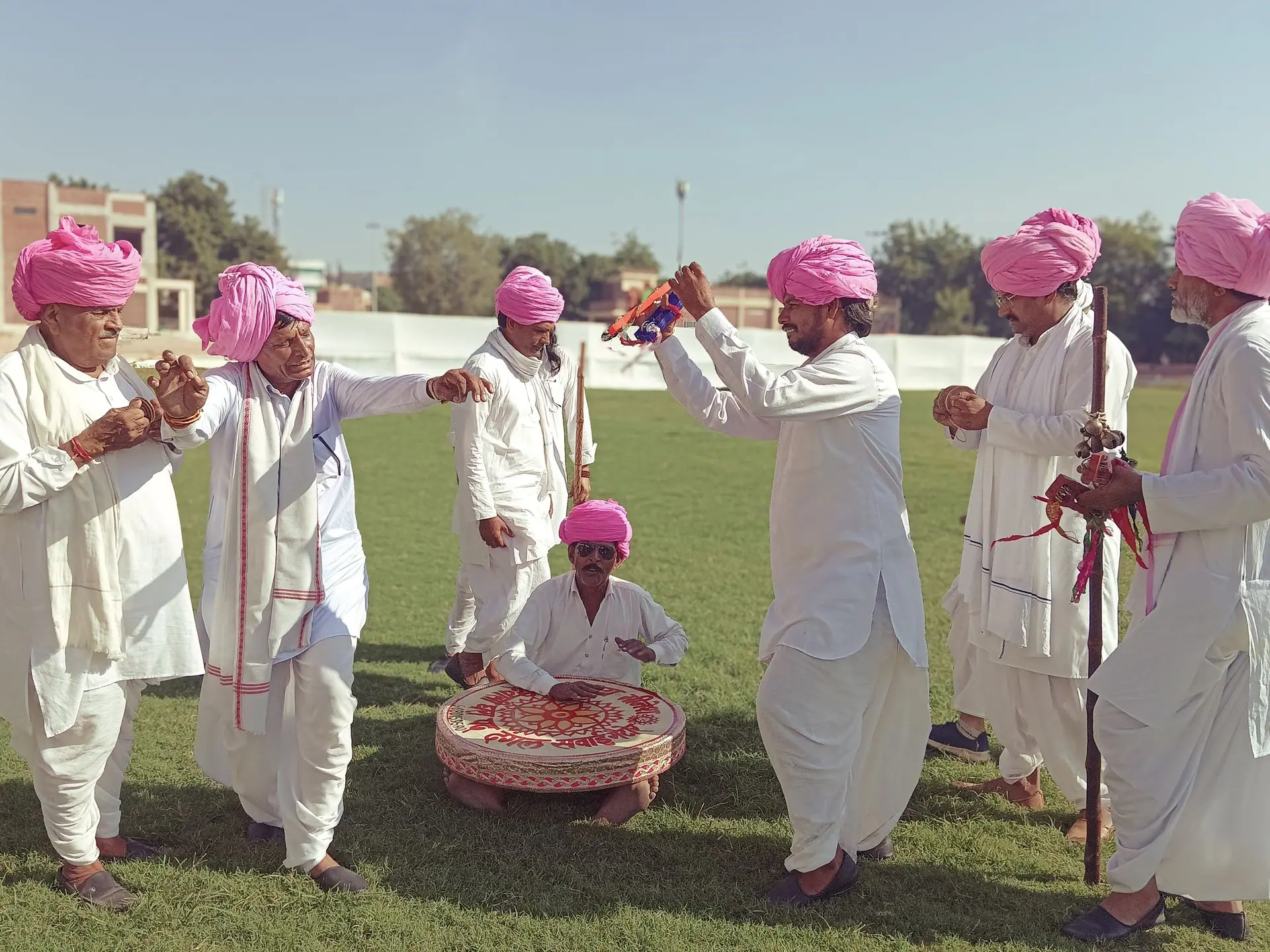 Group of Rajasthani men in vibrant pink turbans performing a traditional folk dance outdoors