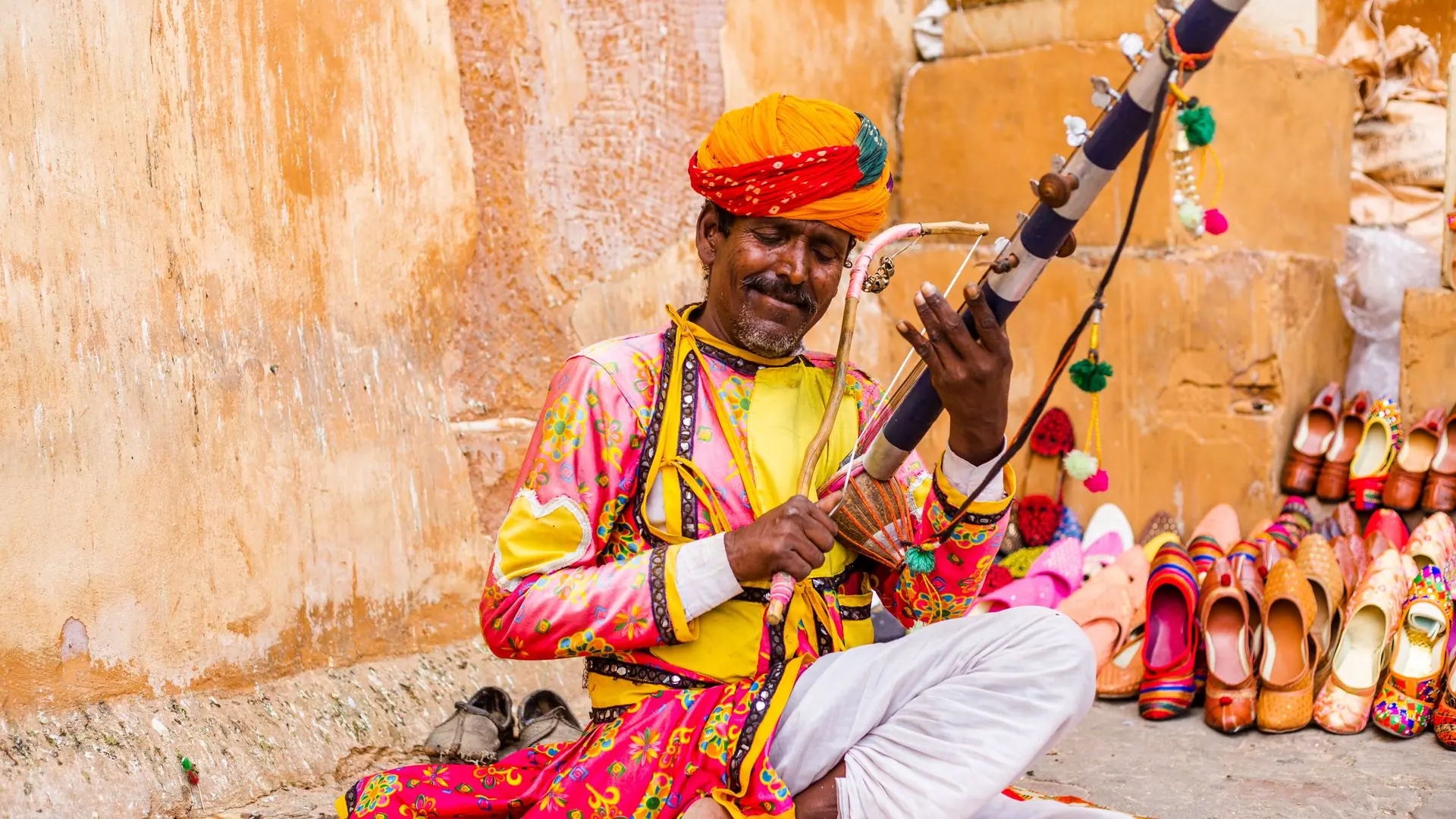 A colorful Rajasthani folk musician plays a traditional instrument outdoors
