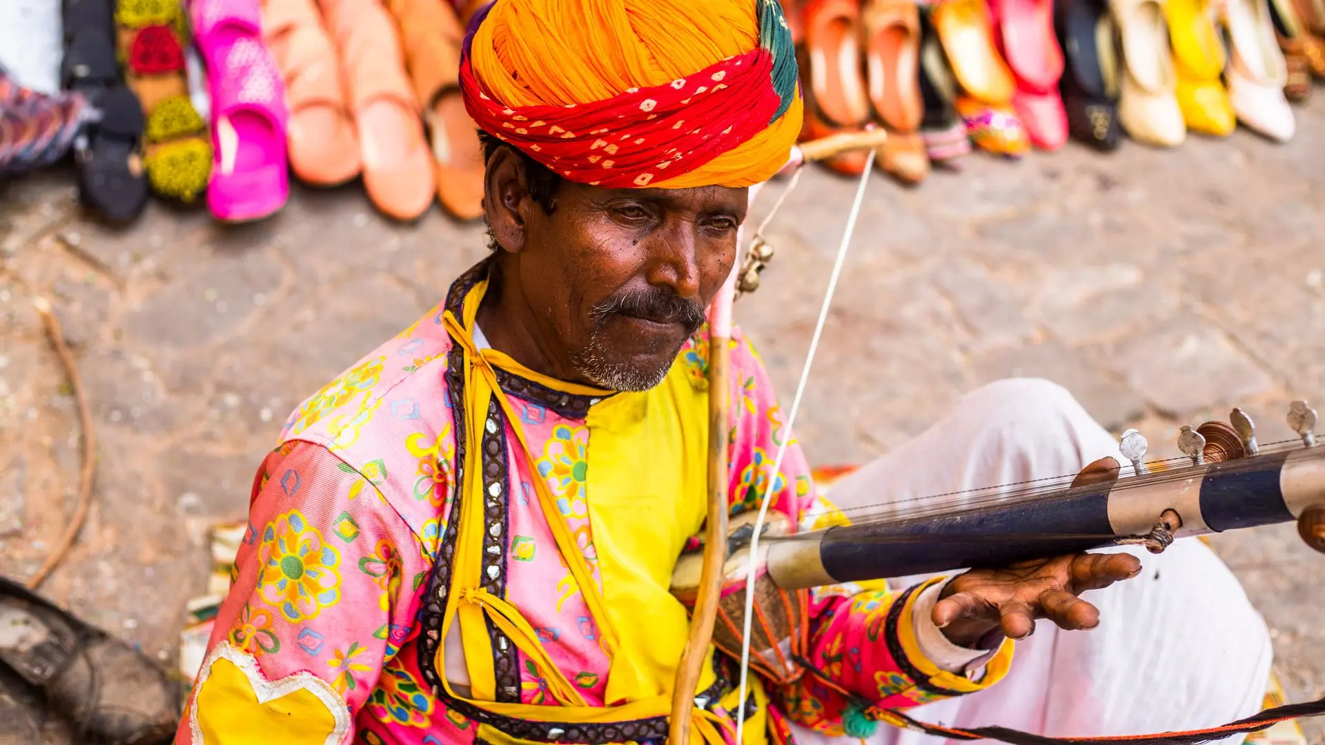Traditional Rajasthani musician playing an instrument outdoors at a cultural event