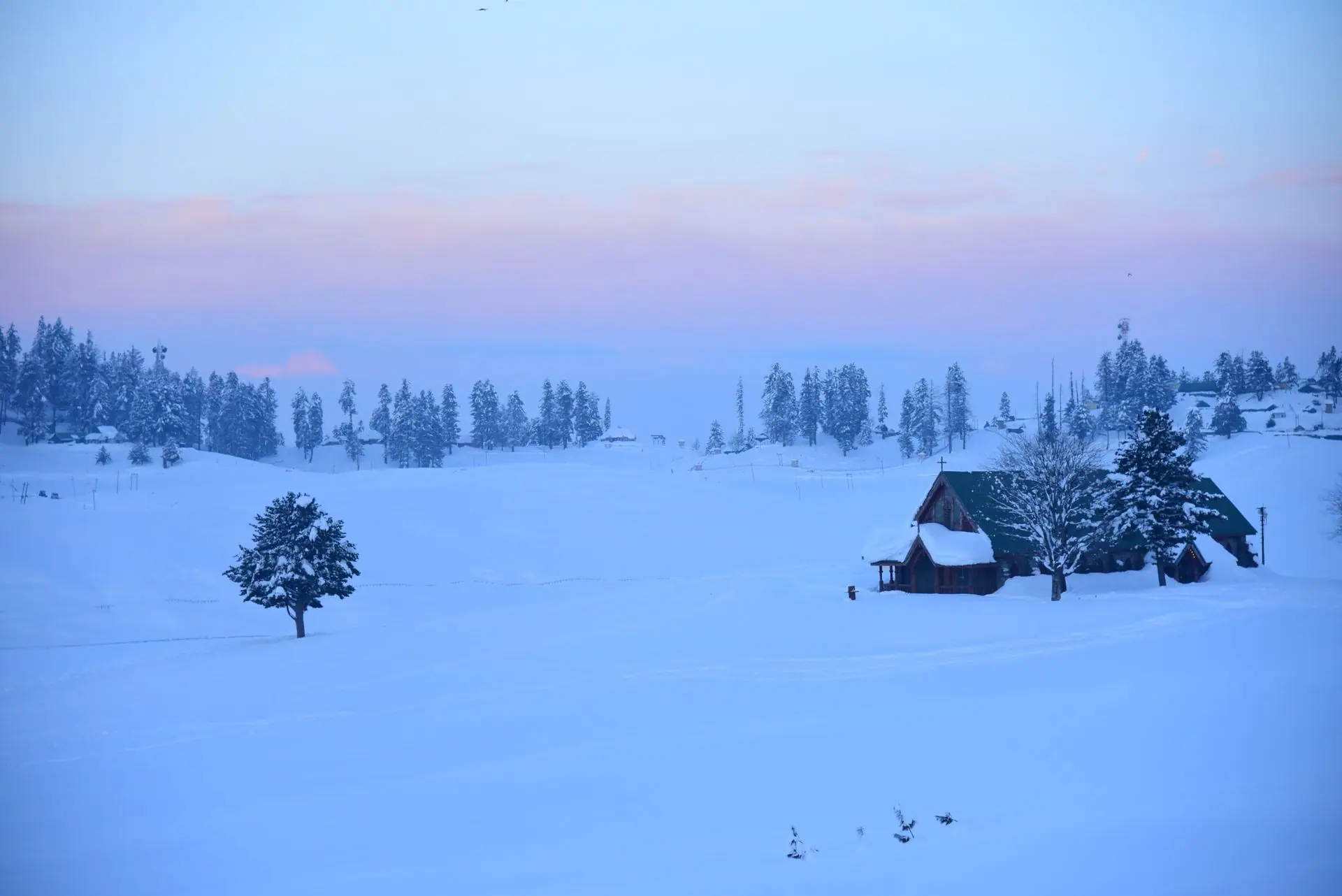 A tranquil winter scene in Gulmarg showcasing snow-covered landscapes and a quaint house during sunset