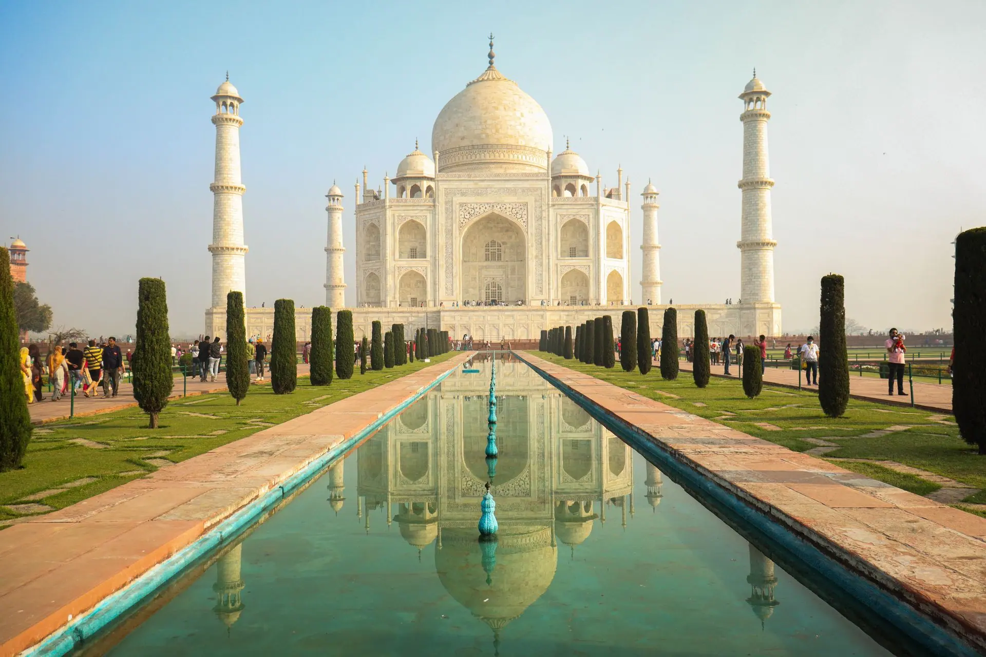The iconic Taj Mahal stands majestically with its reflection in a serene pond, surrounded by lush gardens