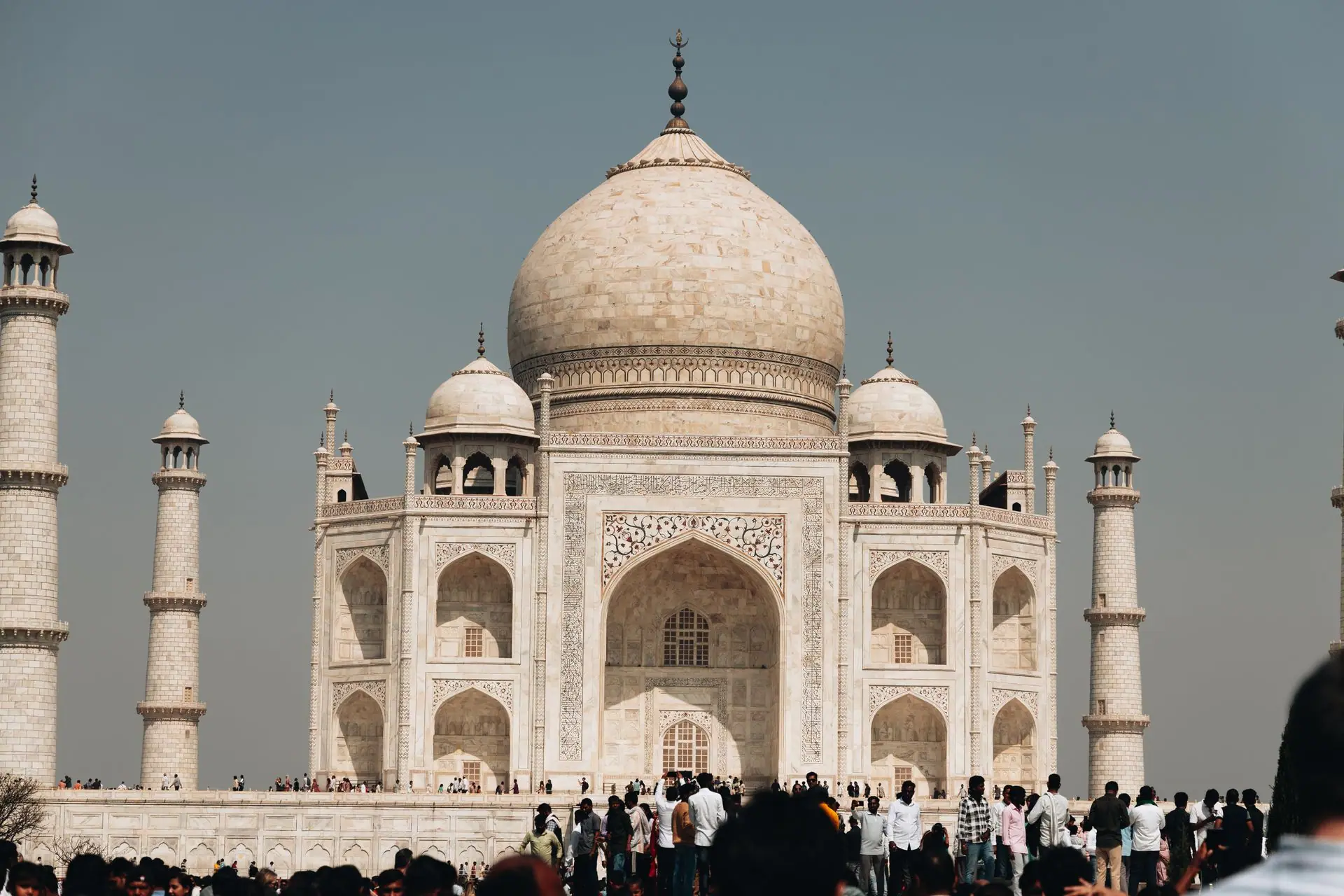 A bustling crowd gathers in front of the majestic Taj Mahal under a clear sky