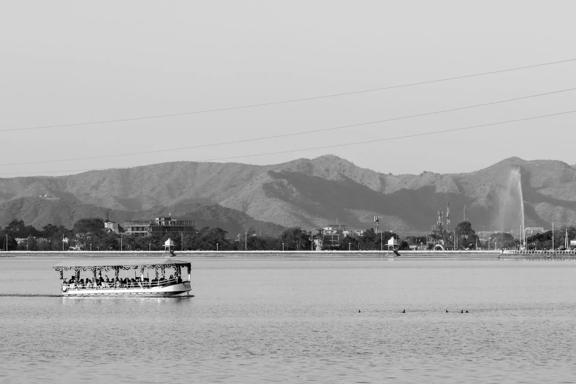 A black and white view of a boat on Lake Pichola with mountains in Udaipur, India