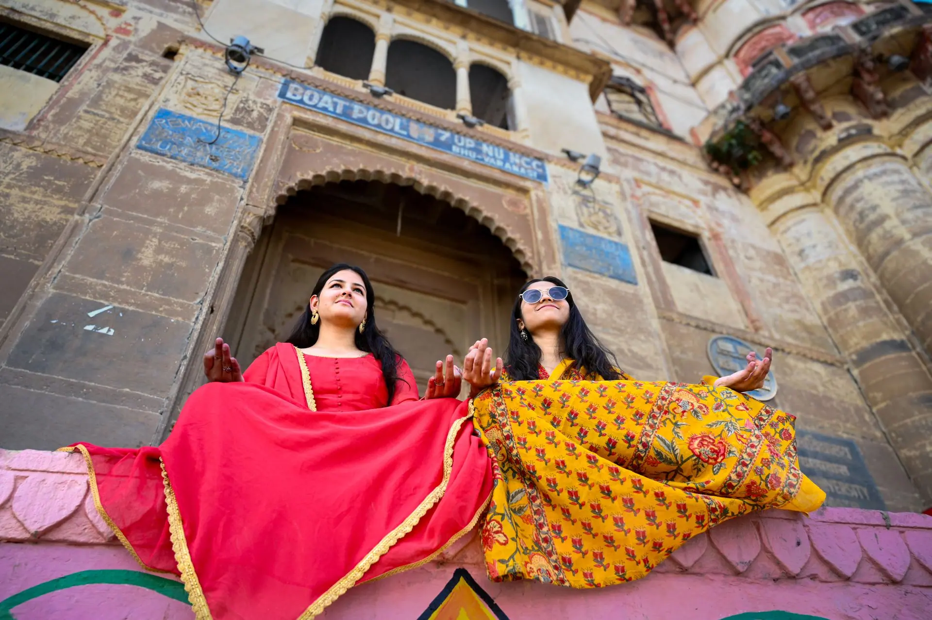 Two women in colorful traditional attire meditating at a historic ghat in Varanasi