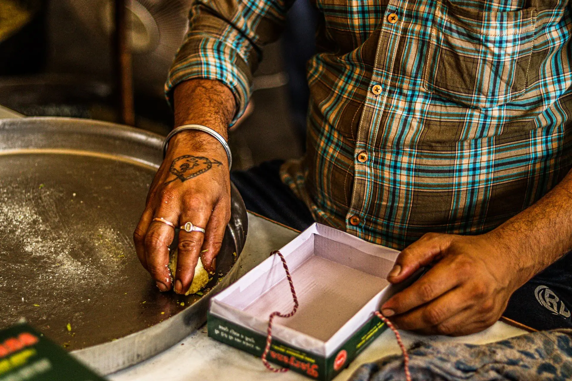 Street vendor shaping and boxing traditional Indian sweets with focus on hands and details