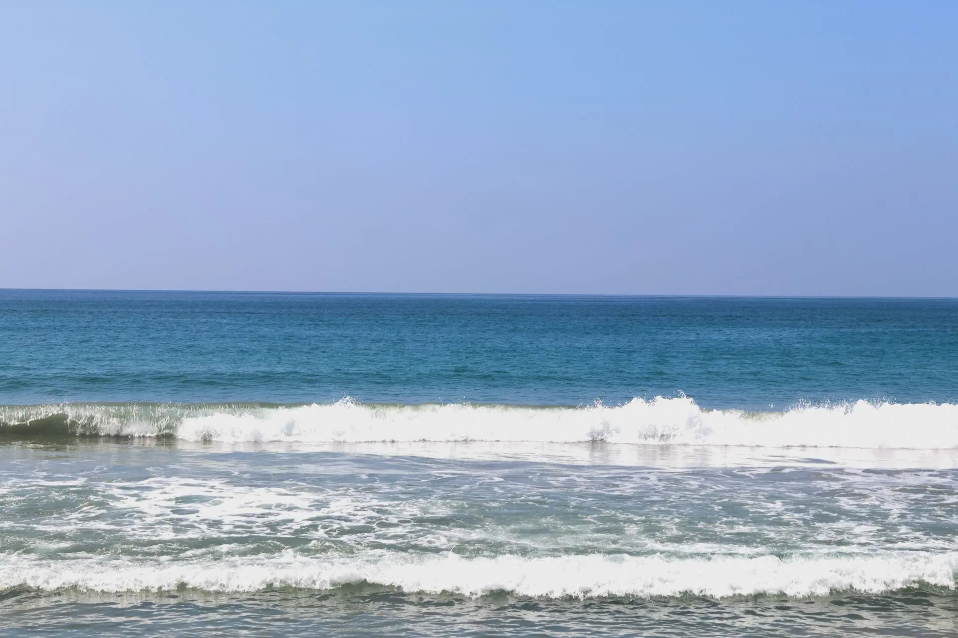 Peaceful ocean waves gently crashing at Varkala Beach, Kerala, India under a clear blue sky