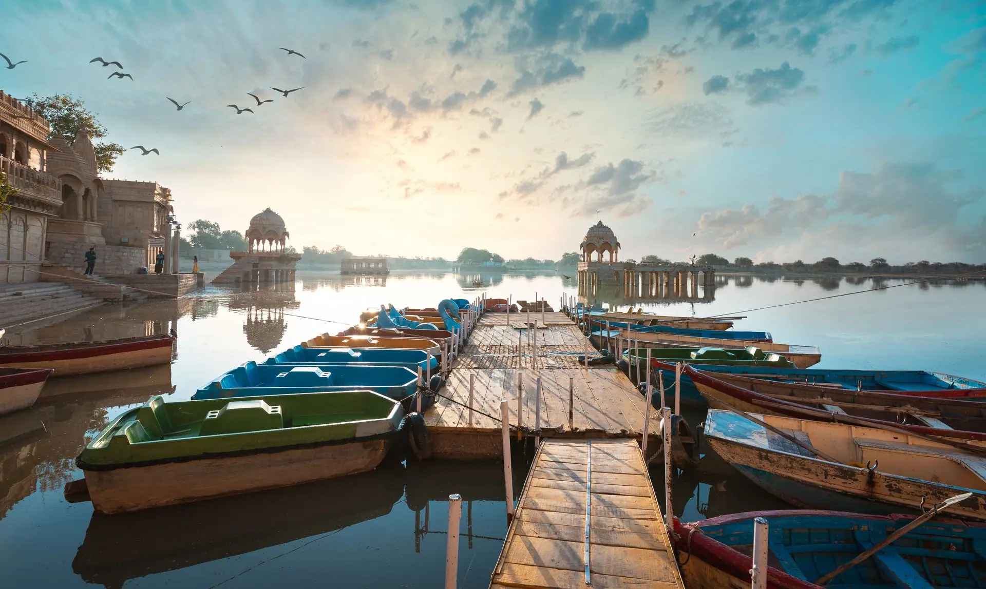 Colorful boats docked at Gadsisar Lake with scenic sunset in Jaisalmer, India