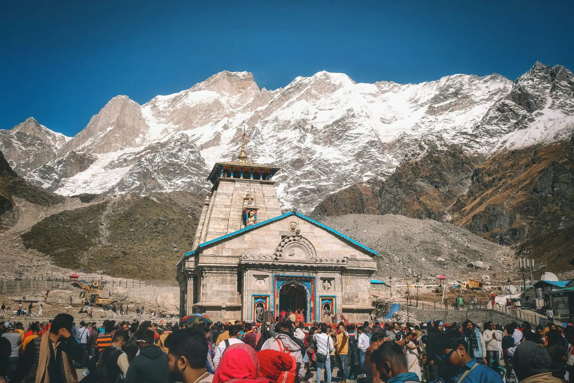 A crowd of pilgrims at Kedarnath Temple with snowcapped Himalayan peaks in the background