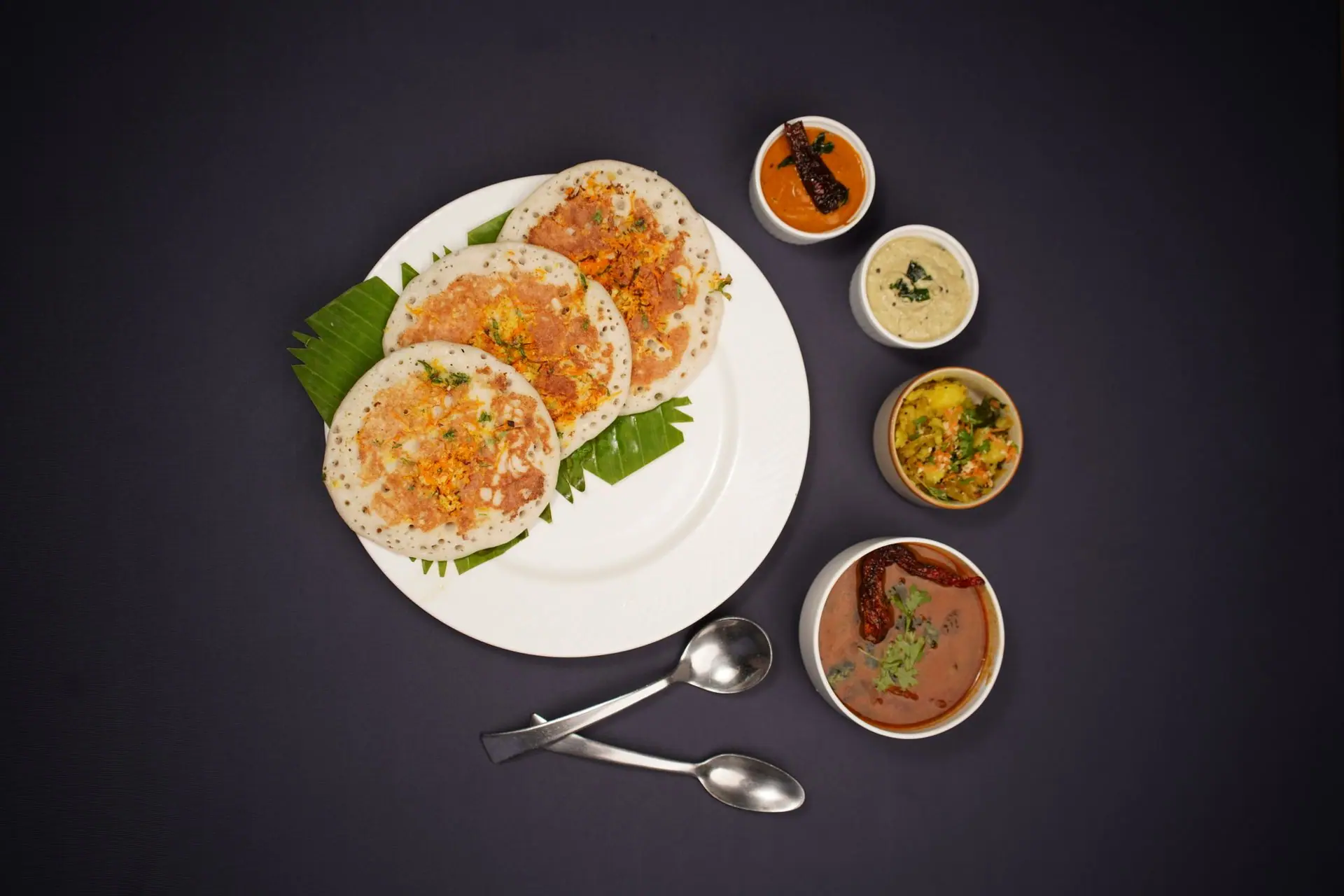 Top view of South Indian dosa served with a variety of chutneys on a black background