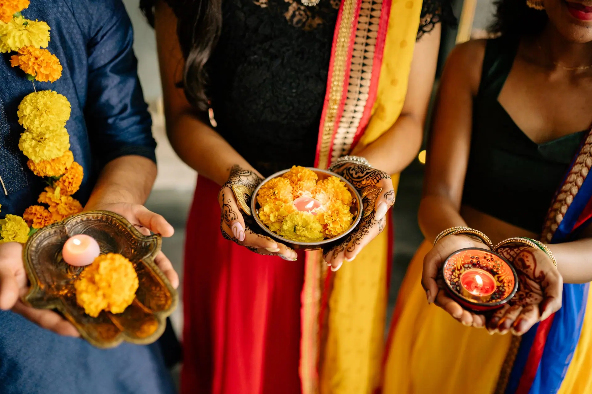 Three people hold traditional Diwali candles and flowers, highlighting Indian culture and celebration
