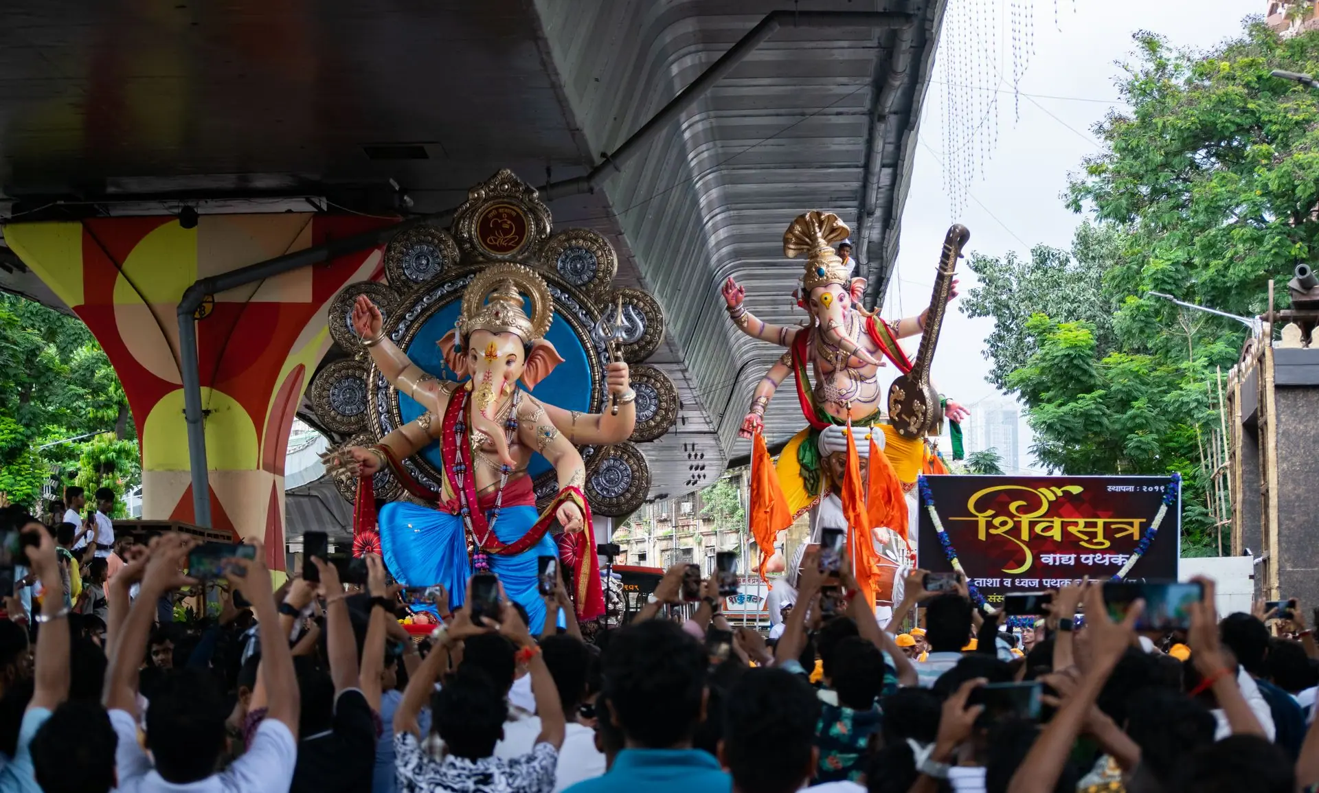 Vibrant scene from Ganesh Chaturthi parade in Mumbai with statues and crowds under a flyover