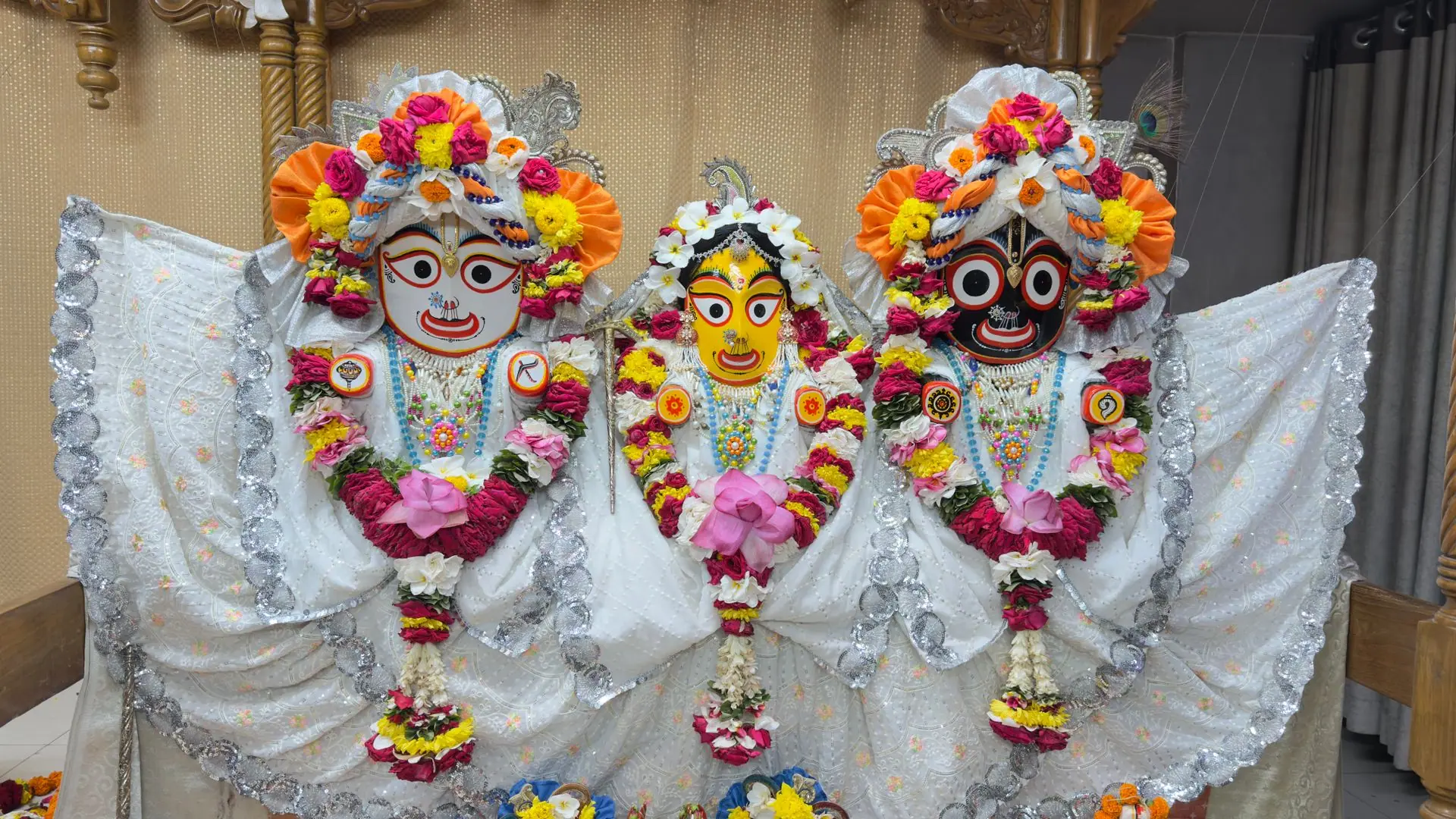 Vibrant Jagannath, Balabhadra, and Subhadra idols adorned with flowers and ornaments indoors