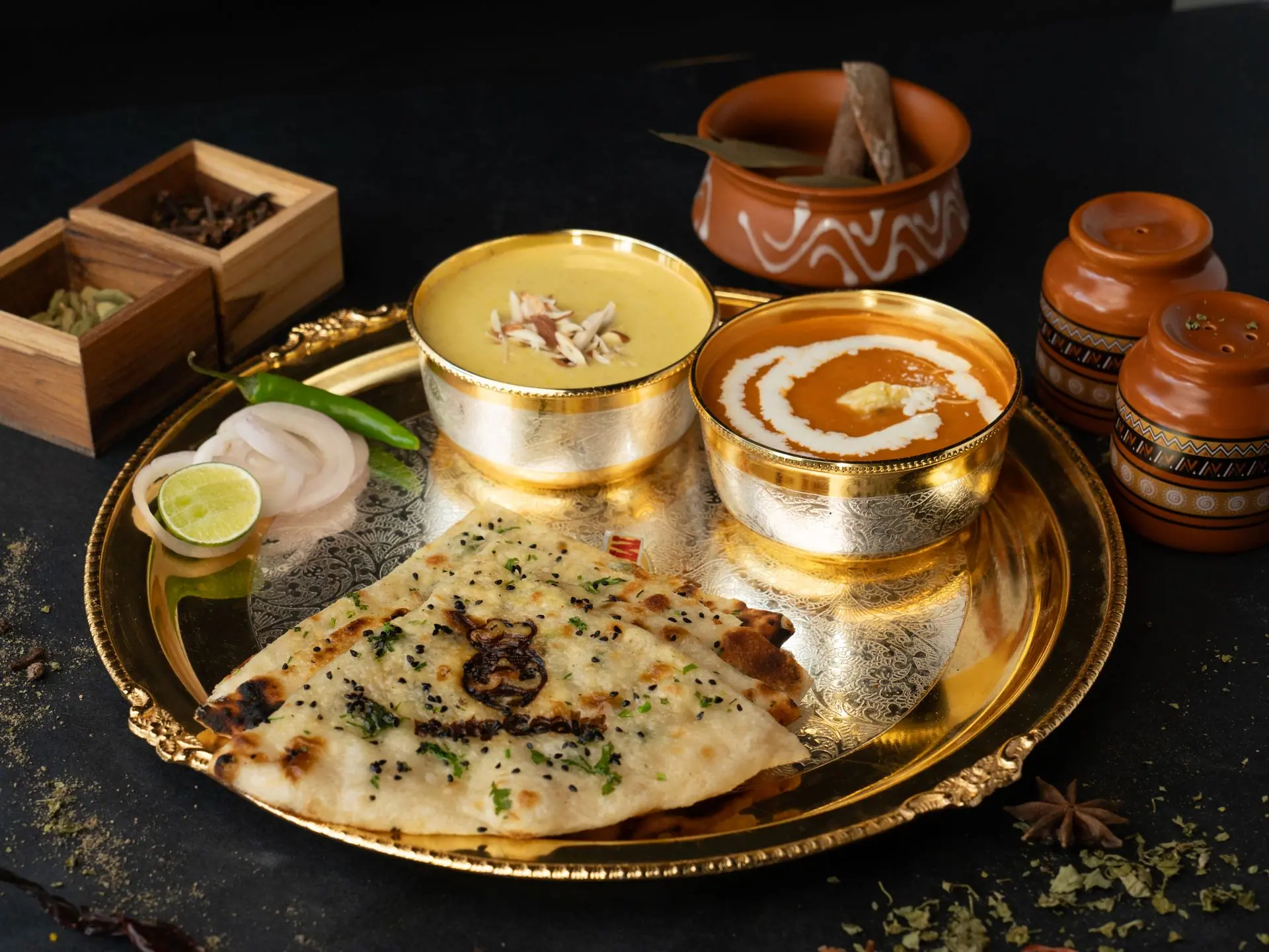 A delectable Indian thali featuring dal, butter chicken, and naan on a golden platter