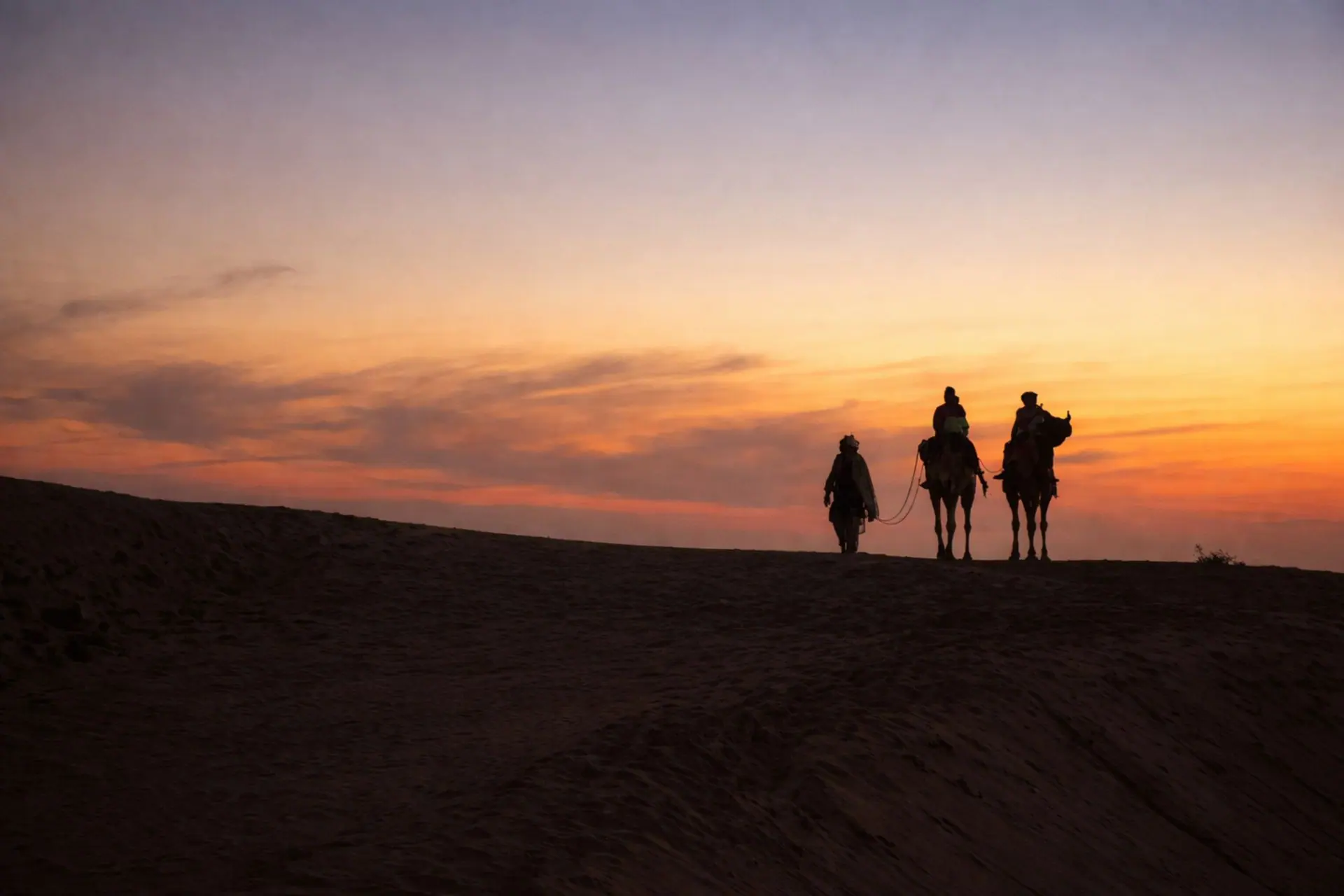 Silhouette of camels and riders during sunset in Sam, Rajasthan's Thar Desert