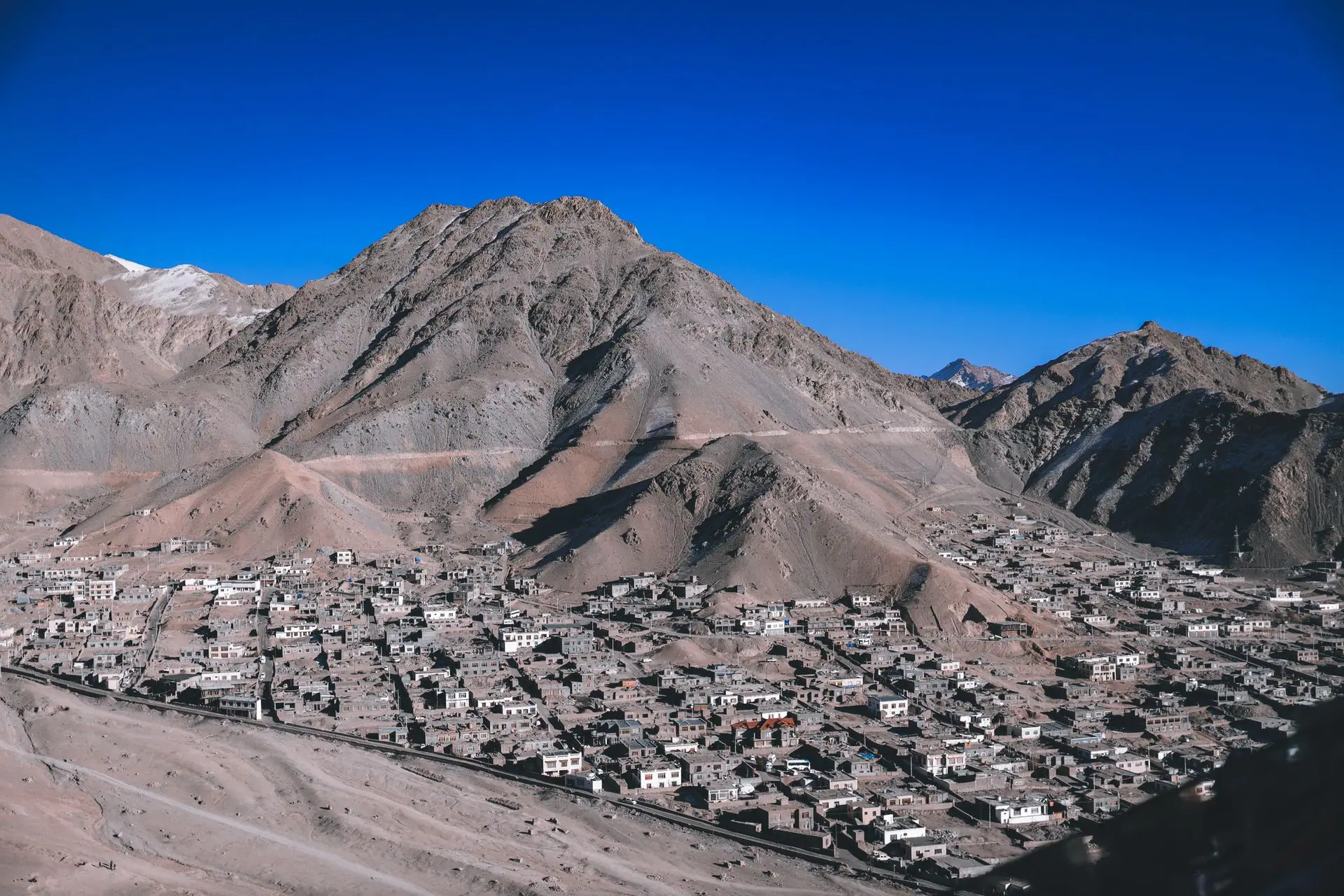 A stunning aerial view of Leh with its rugged mountain backdrop and scattered village buildings under a clear blue sky